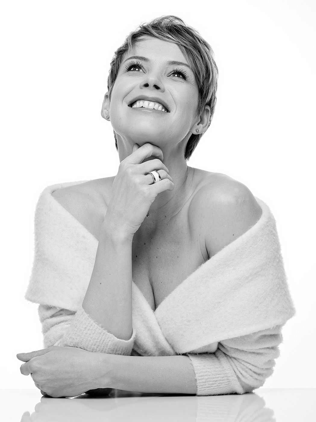 Black and white photo of a smiling short-haired woman in an off-shoulder wrap looking upward.