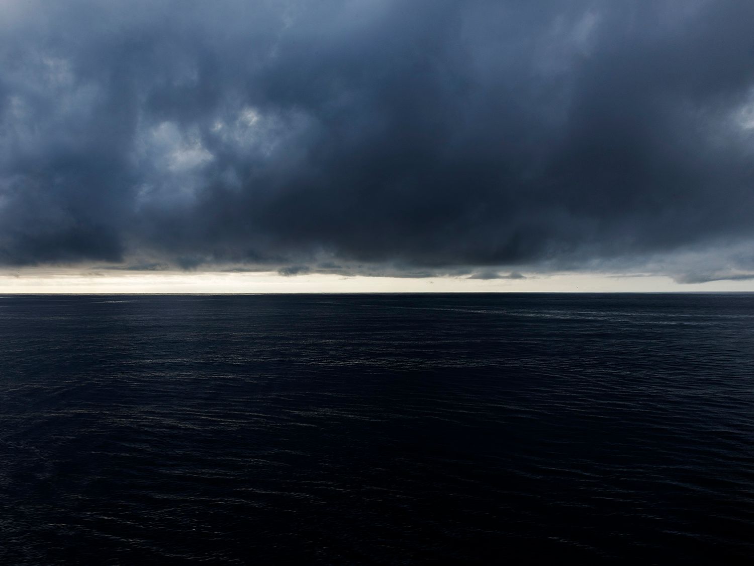Dark stormy clouds loom over a calm, deep blue ocean horizon, creating a dramatic and moody seascape.