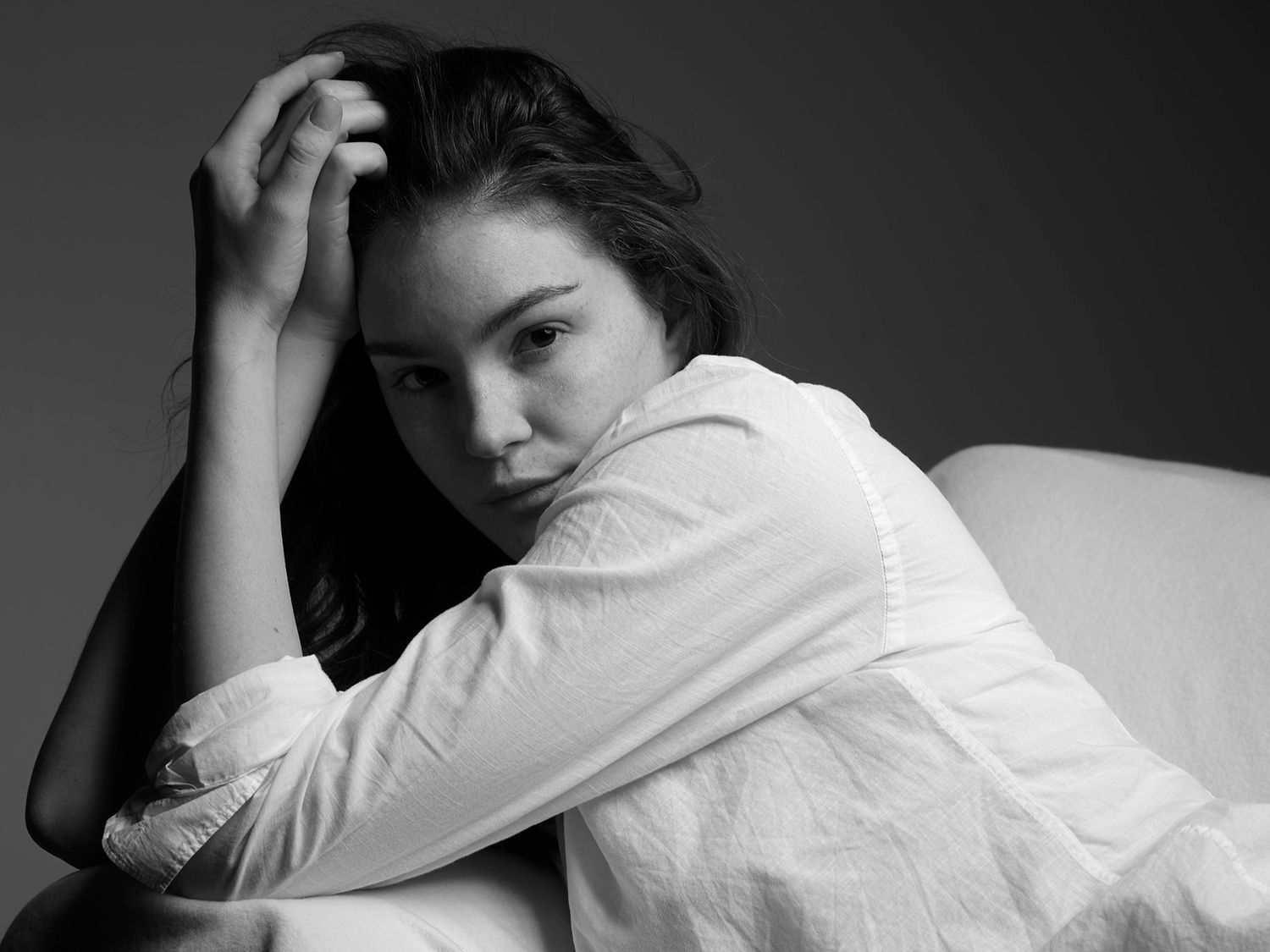 Black and white portrait of a young woman in a white shirt, resting her head on her hand thoughtfully.