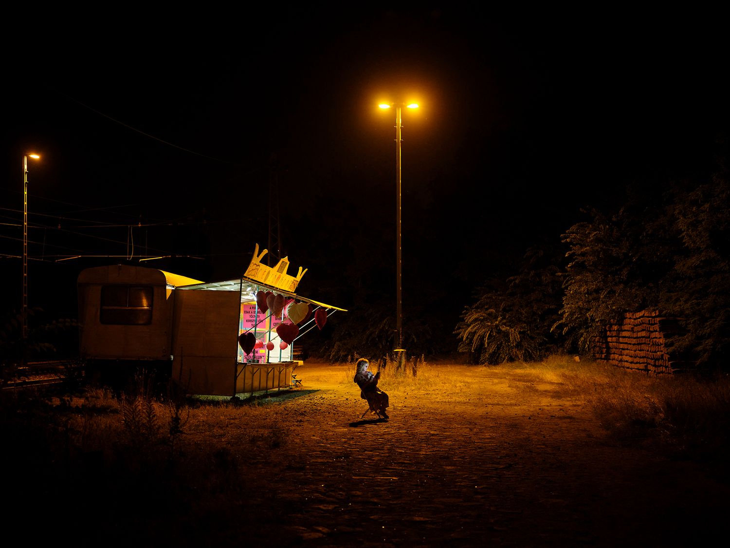 A colorful illuminated food stall glows under street lights on a dark empty lot at night.