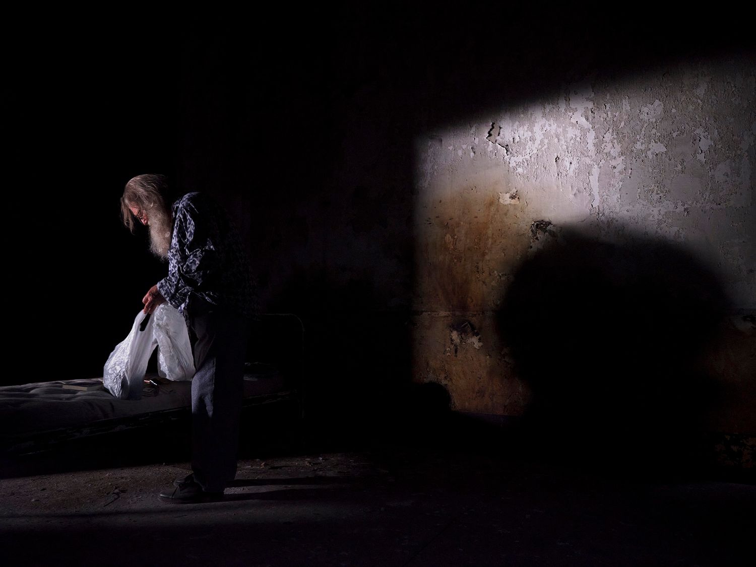 Solitary figure walking near a spotlight on a dark textured wall.