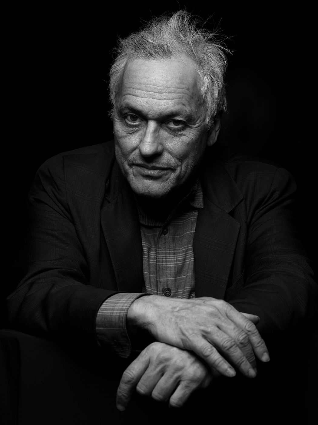 Black and white portrait of an older man with white hair in a dark blazer, hands clasped together. Marc Ribot