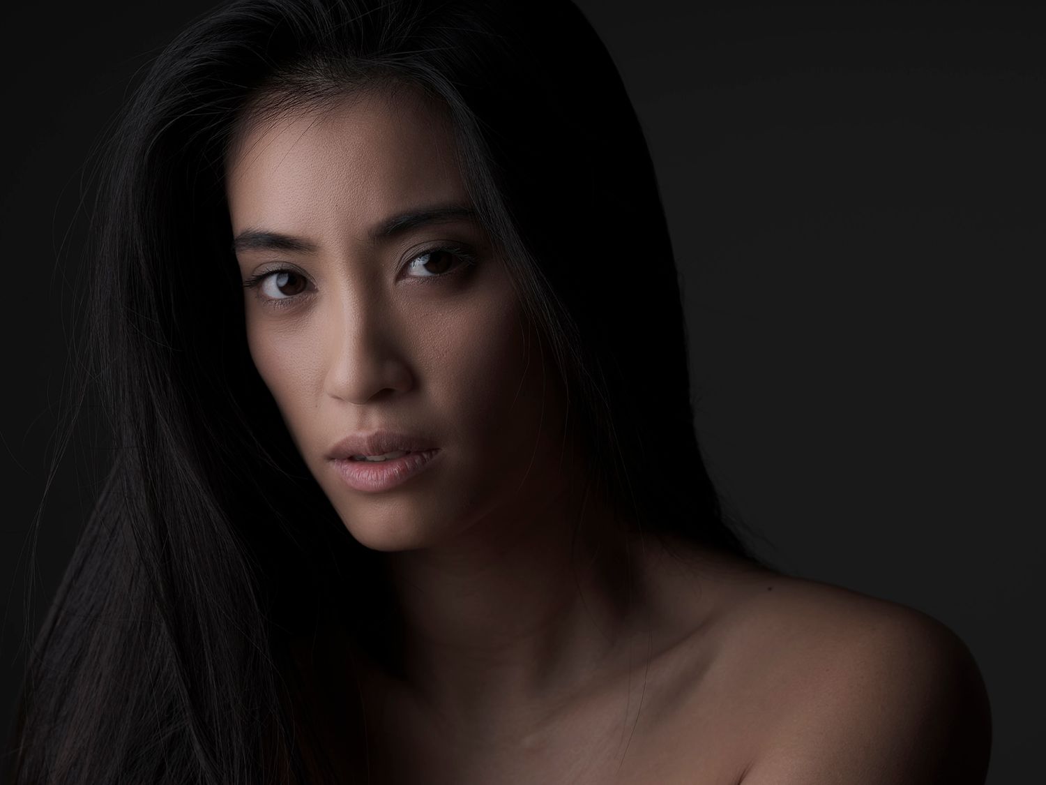 Close-up portrait of a young Asian woman with long black hair against a dark background.