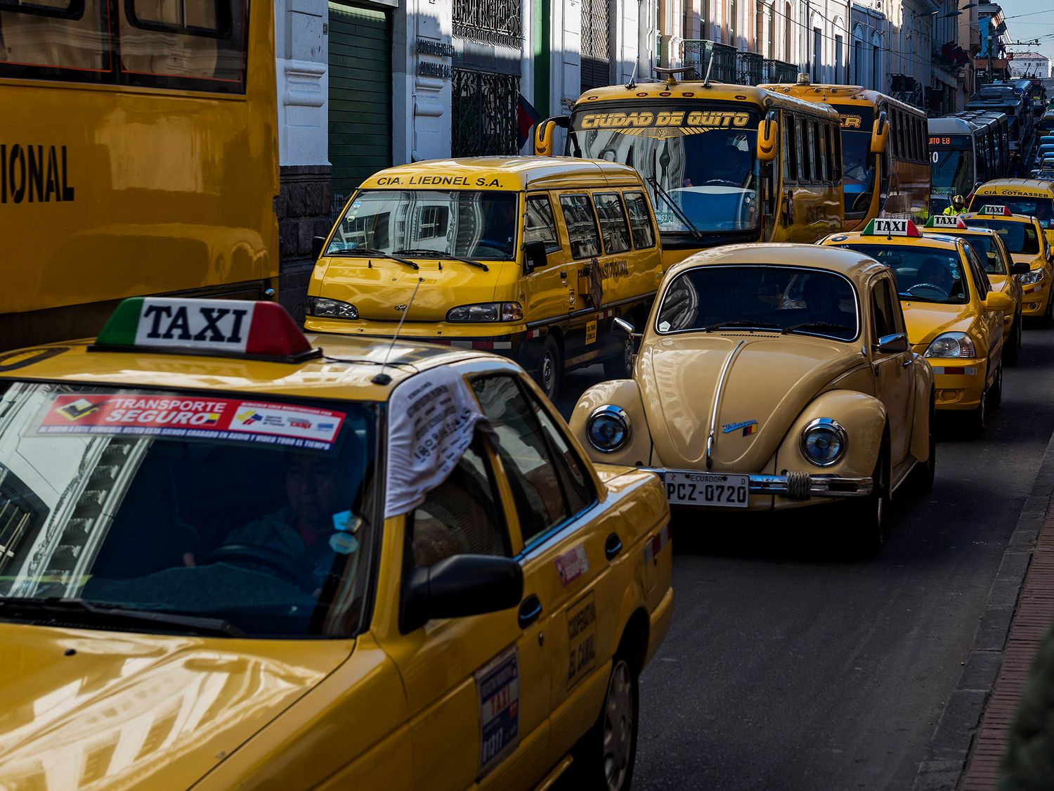 Yellow taxis and a vintage VW Beetle fill a busy street in Quito, Ecuador, with a city bus visible in the background.