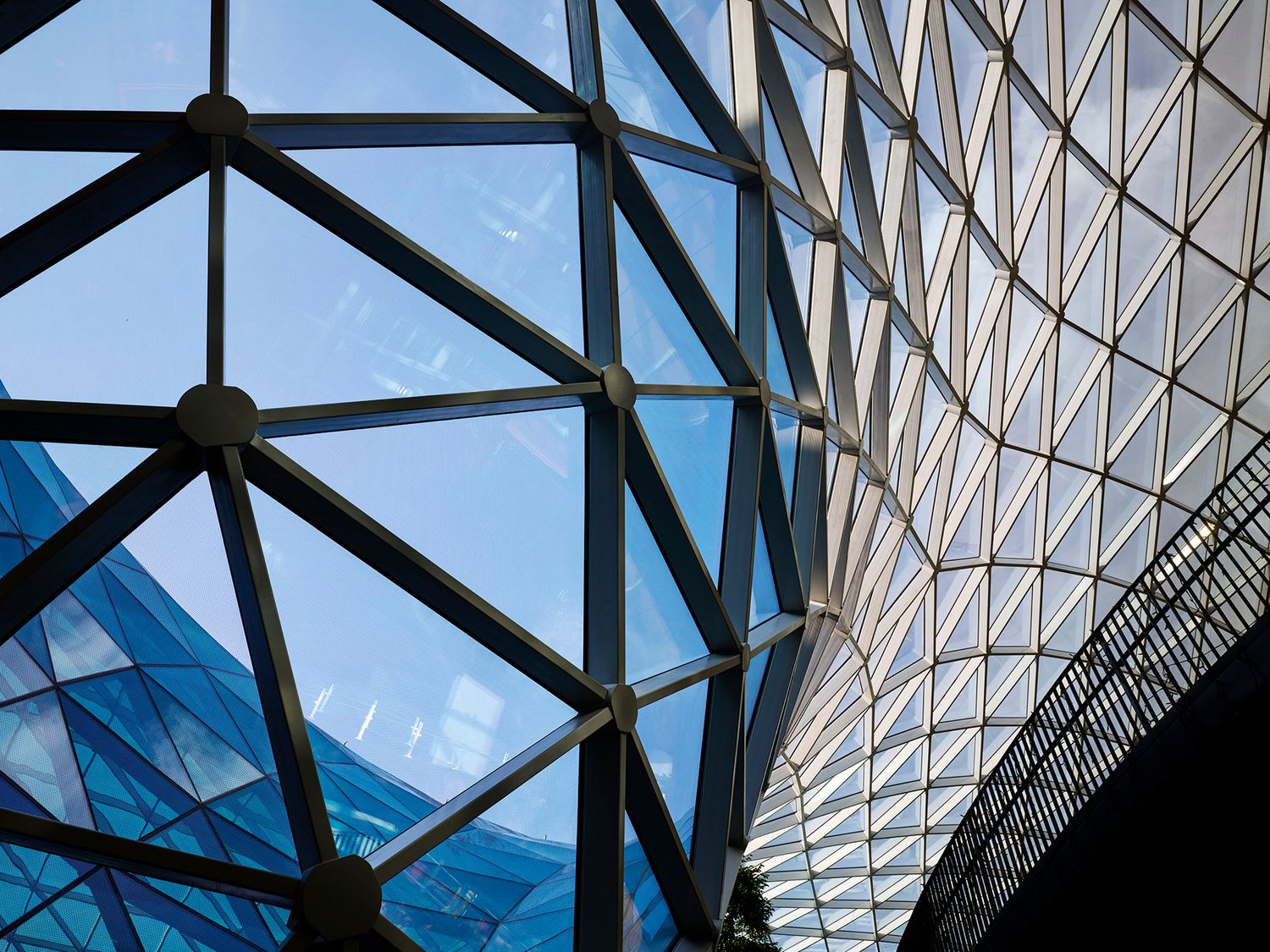 Modern glass and steel architectural ceiling with geometric triangular patterns against a blue sky.