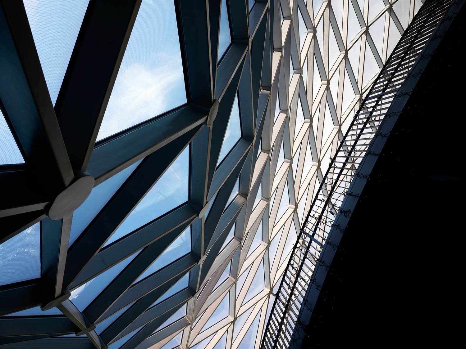 Abstract architectural detail of geometric steel framework and diamond-patterned facade against a blue sky.