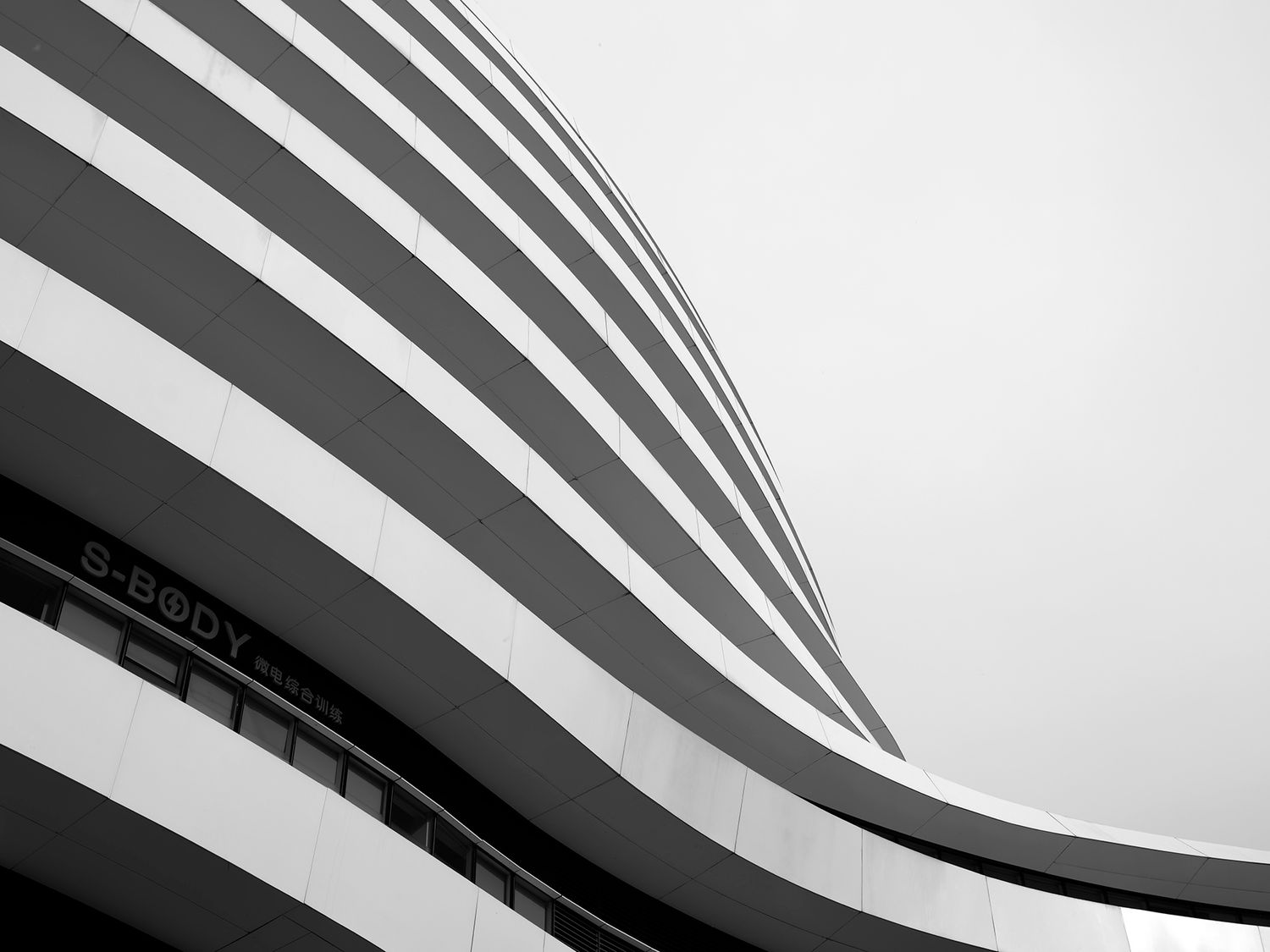 Black and white architectural photo of a curved modern building with bold horizontal stripes against a pale sky.