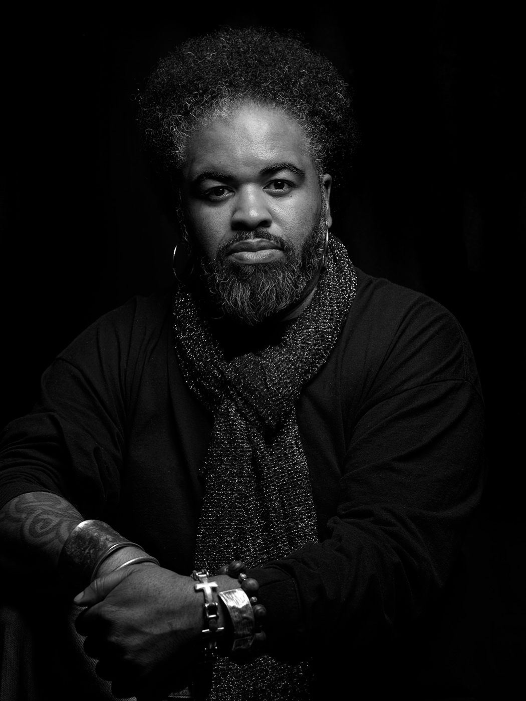 Black and white portrait of a bearded man with natural hair, wearing a scarf and black jacket, arms crossed. Bobby Sparks