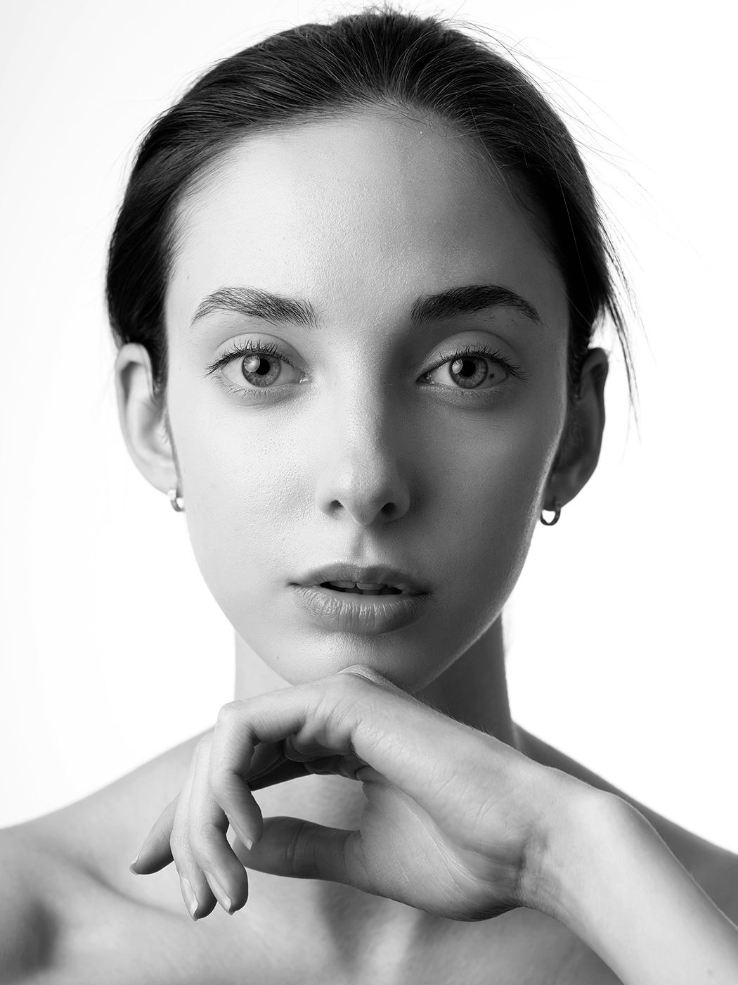 Black and white portrait of a young woman with dark hair, resting her chin on her hand, wearing small hoop earrings.