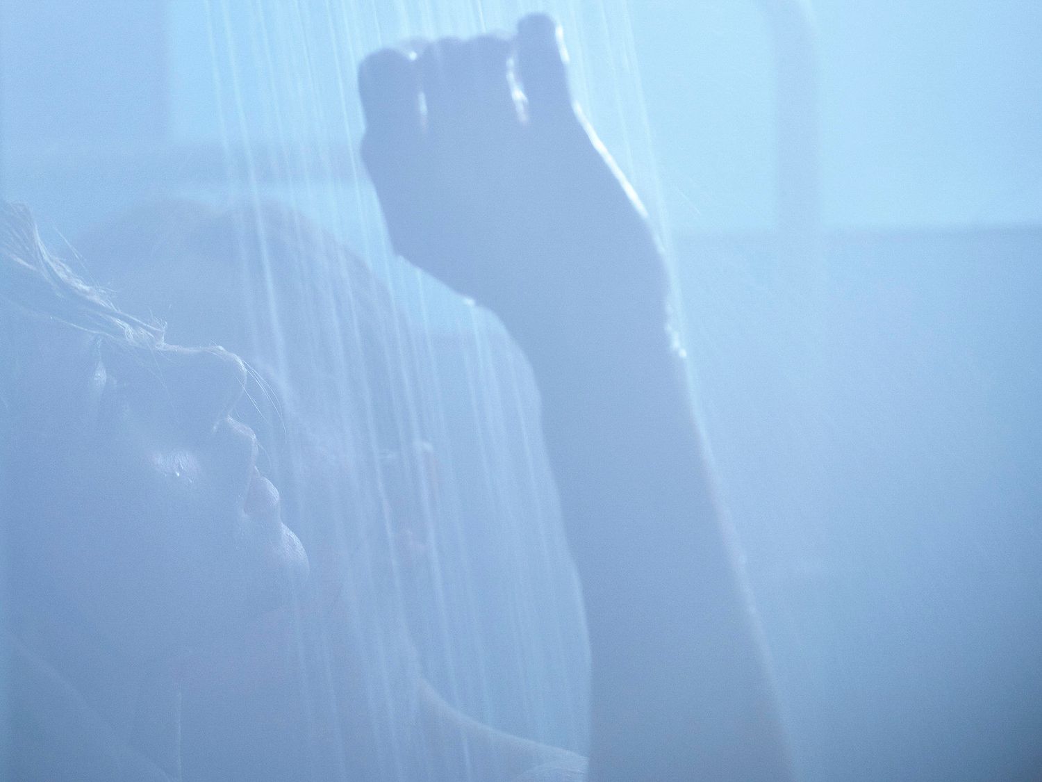 Abstract close-up of hands visible through a sheer curtain in soft blue light.