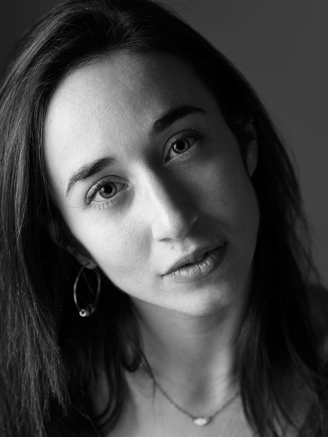 Black and white close-up portrait of a dark-haired woman wearing hoop earrings and a delicate necklace.