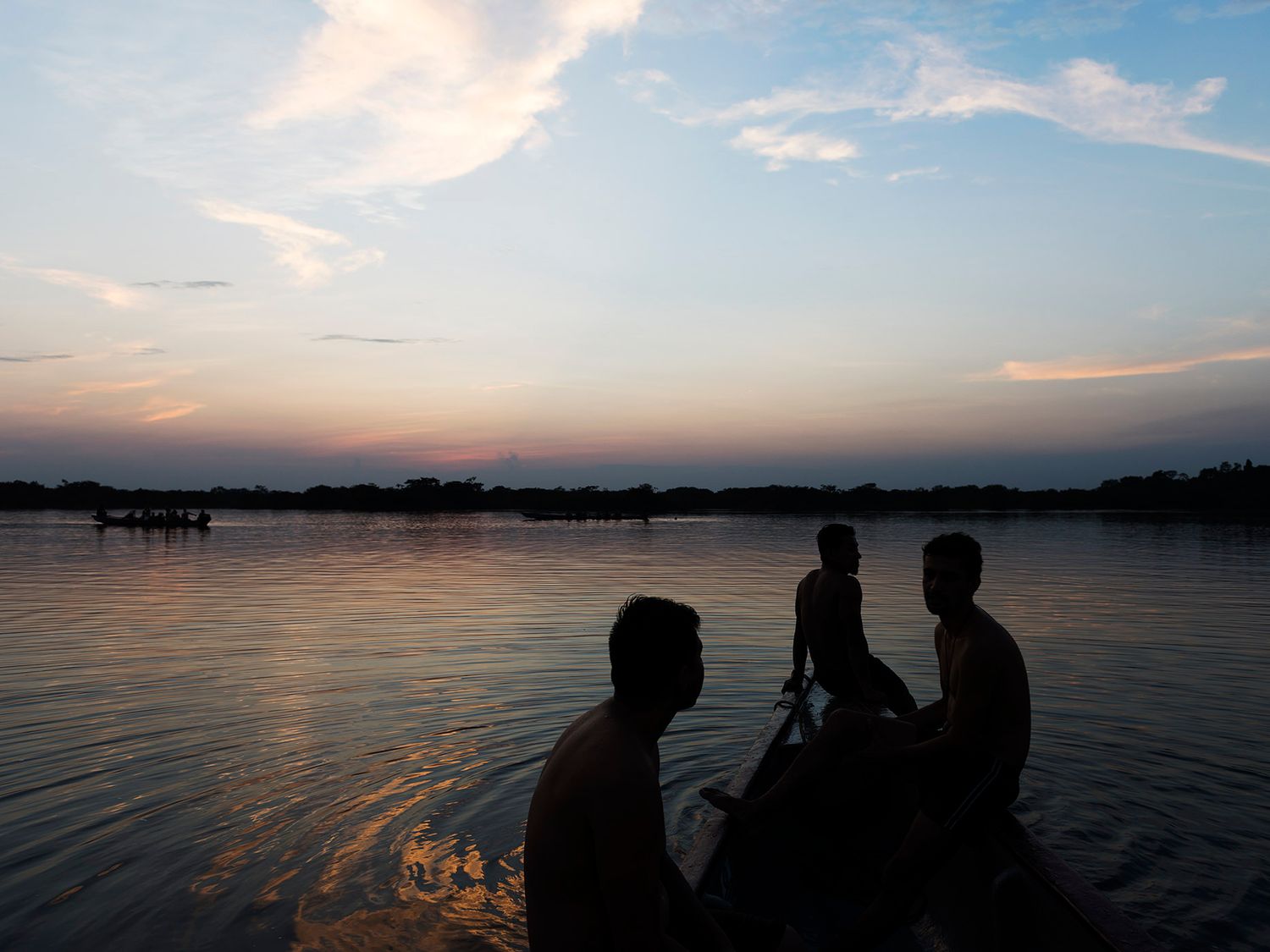 Silhouettes of people on a boat during a serene river sunset with colorful sky.