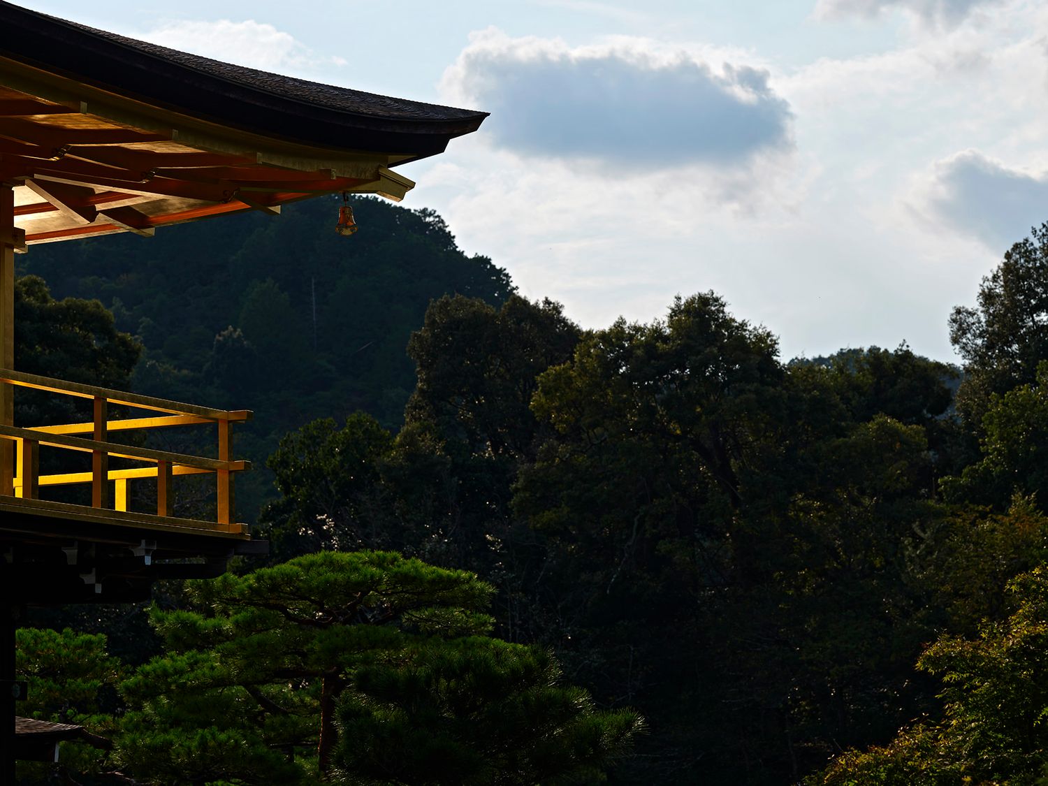 Golden pavilion roof of Kinkaku-ji temple with lush green trees and misty mountain backdrop in Kyoto, Japan.