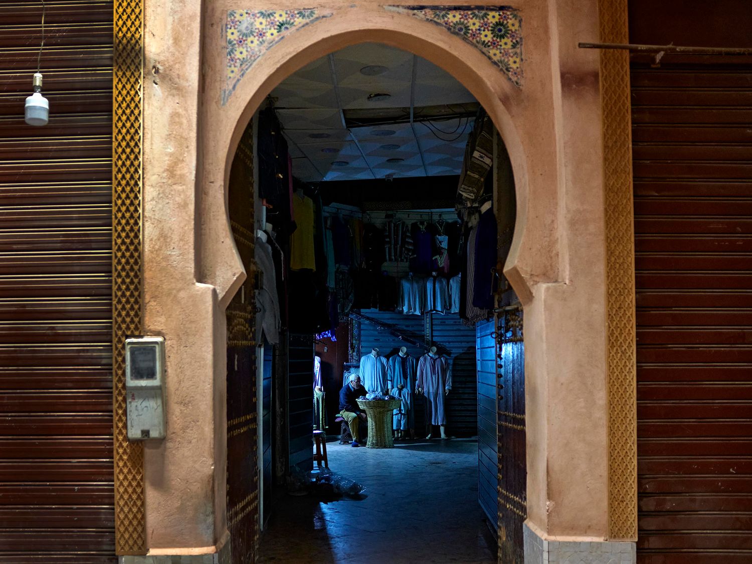 Atmospheric arched doorway in a Moroccan medina at night, revealing a dimly lit alleyway with shops.