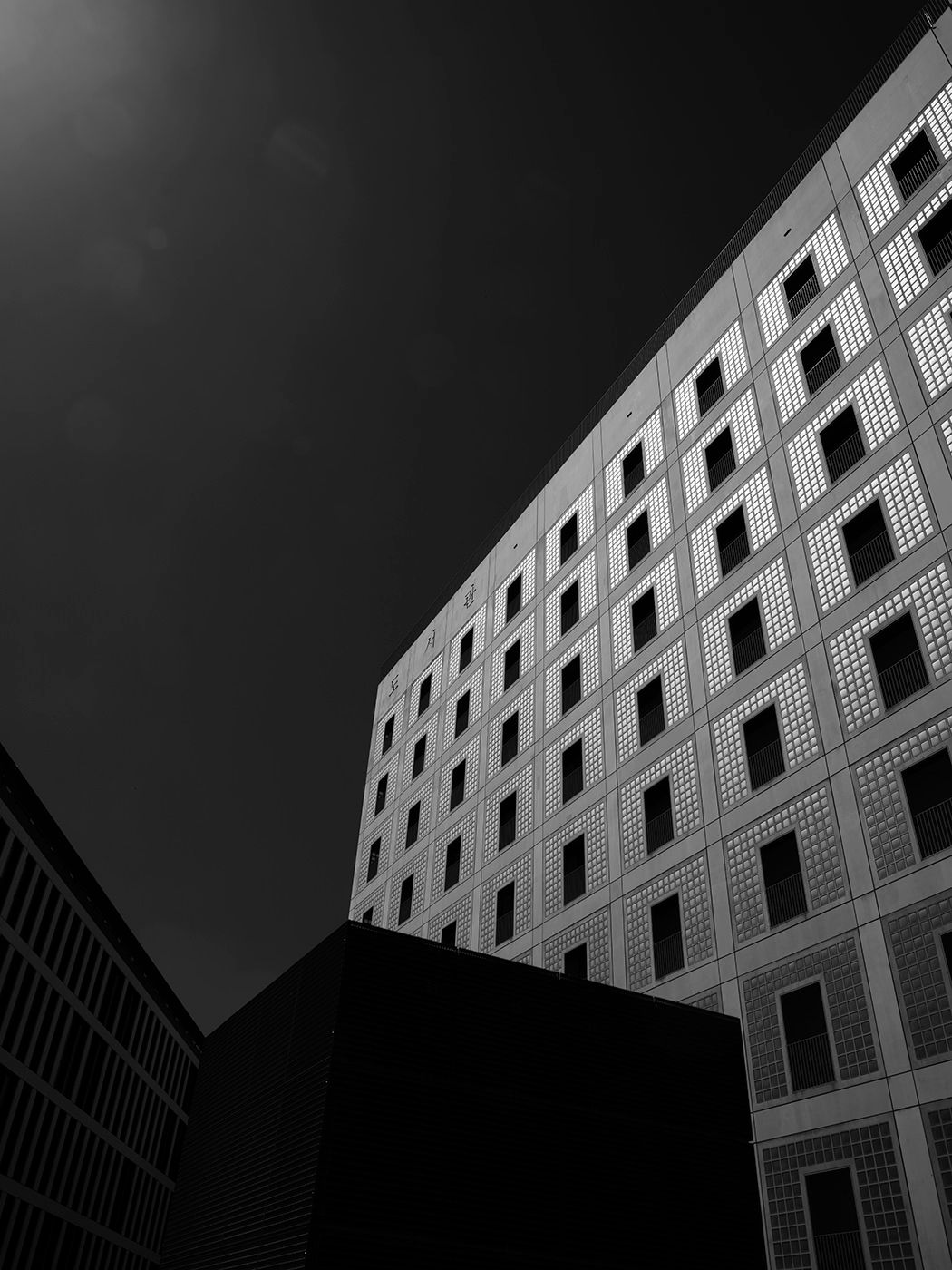 Black and white low-angle photo of modern geometric office buildings against a dark dramatic sky.