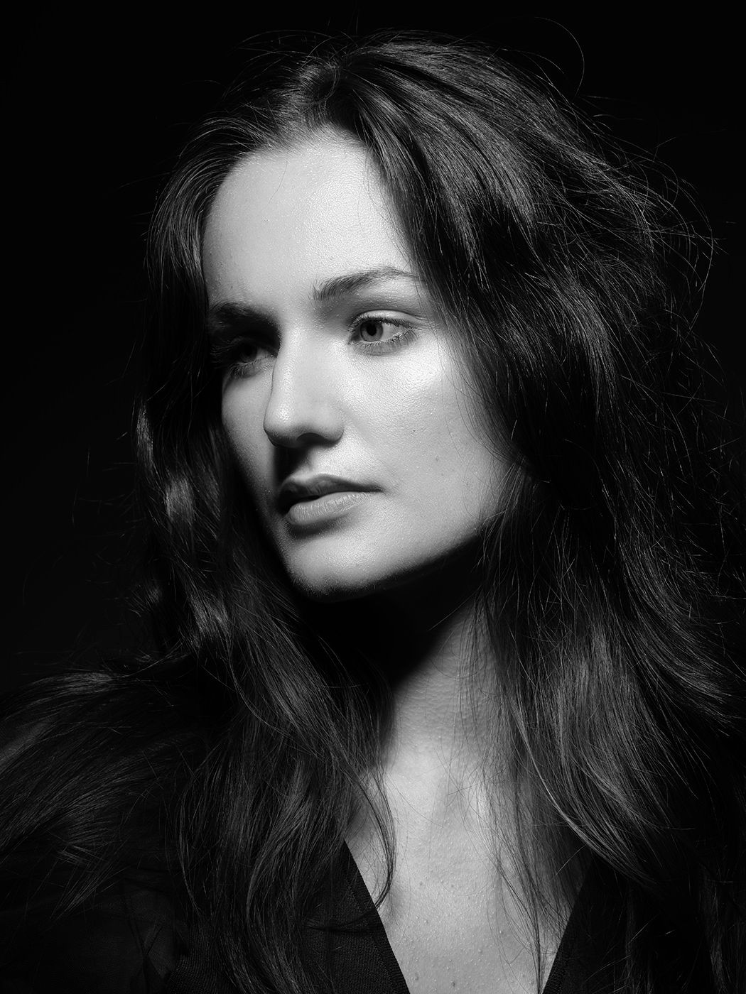 Black and white portrait of a young woman with long dark hair against a dark background.