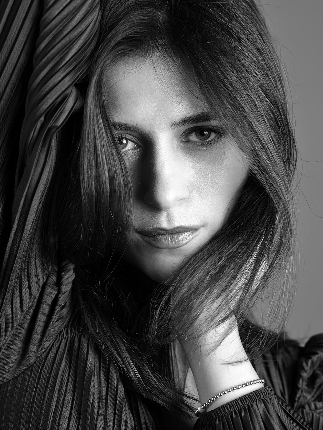 Black and white dramatic portrait of a woman with dark hair partially covering her face in pleated fabric.