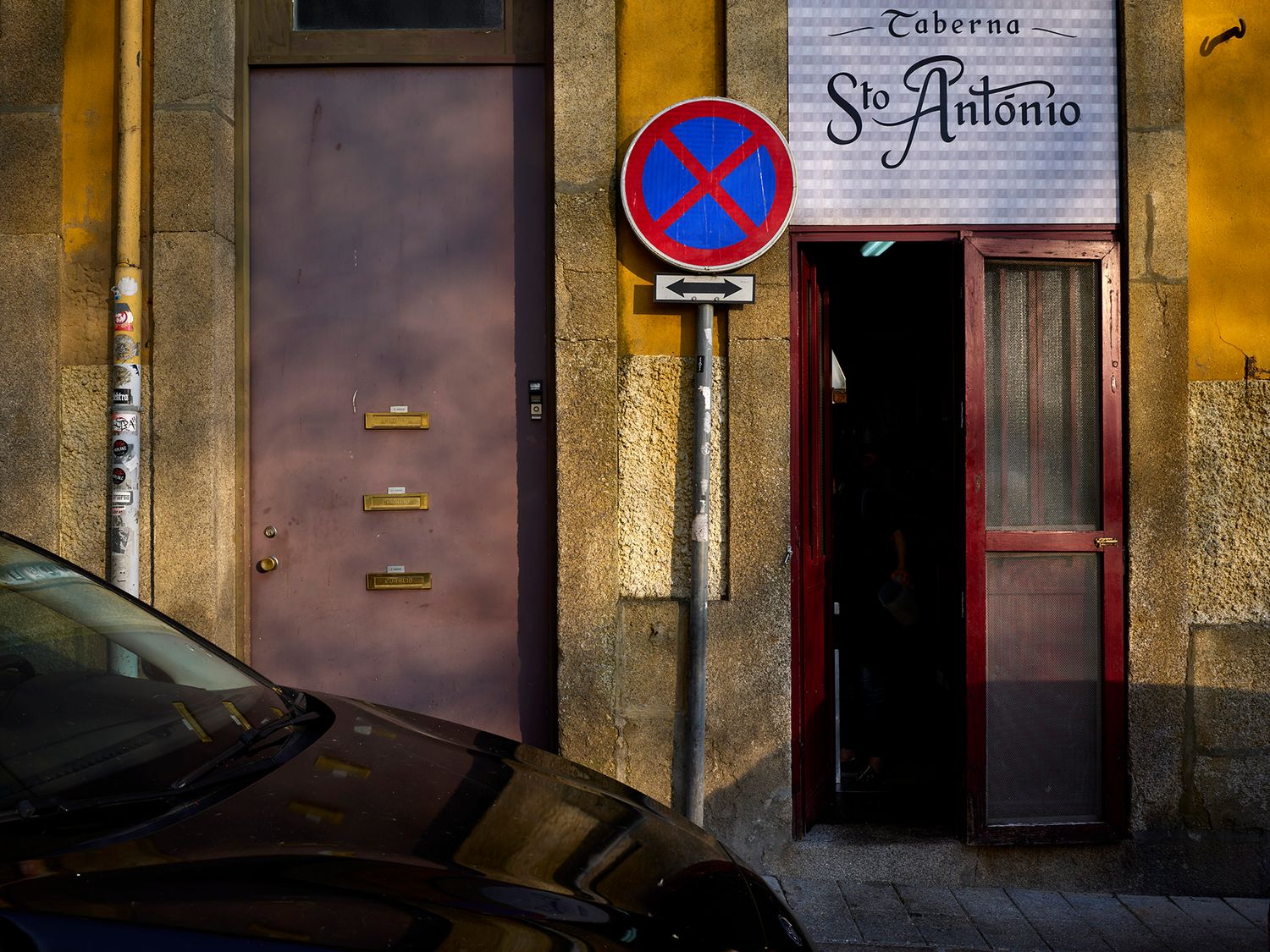 Taberna Sto. Antonio restaurant entrance with red no-parking sign on weathered stone wall in Porto, Portugal.