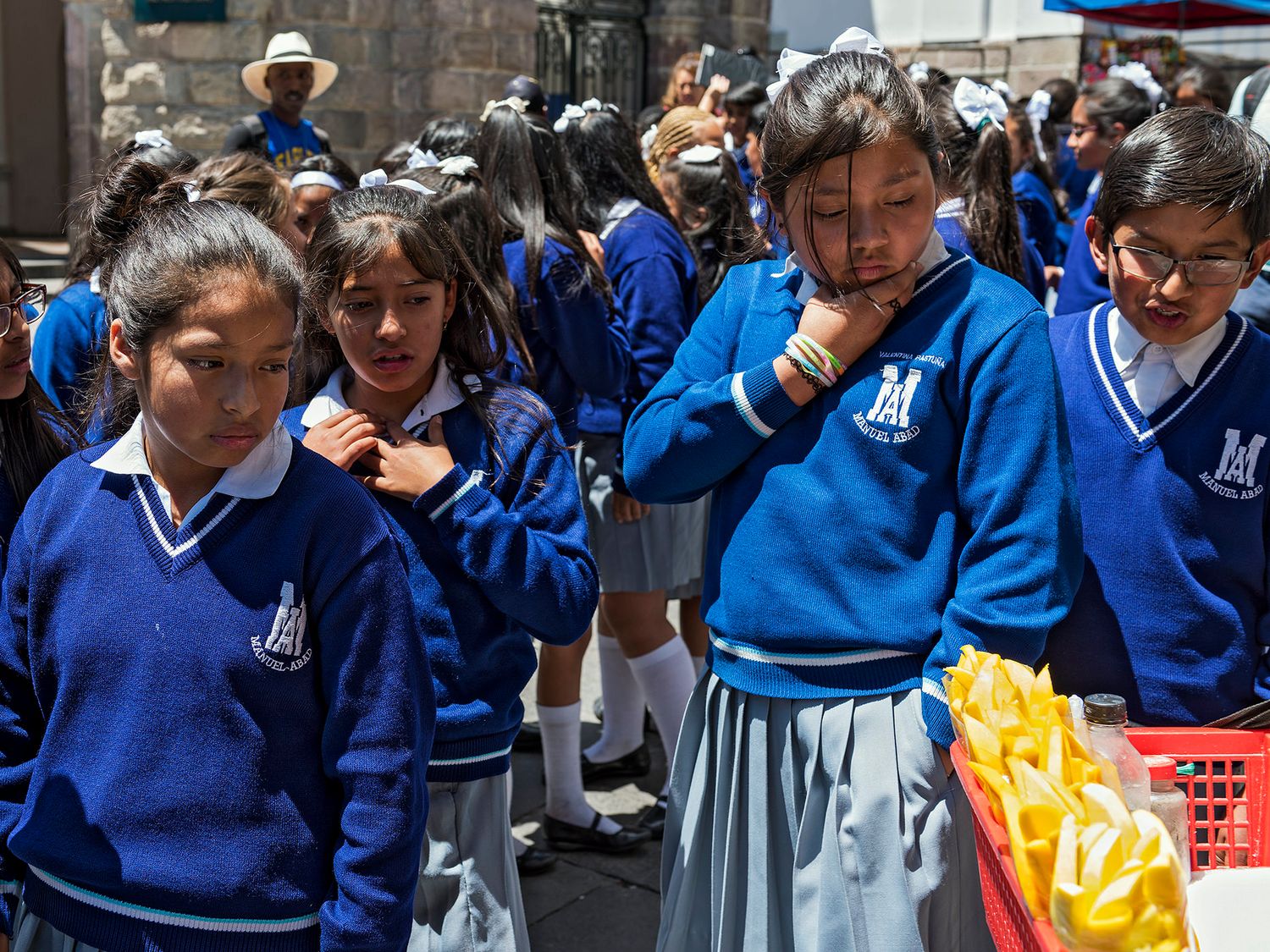 Peruvian schoolgirls in blue uniforms stand outdoors during a school event on a sunny day.