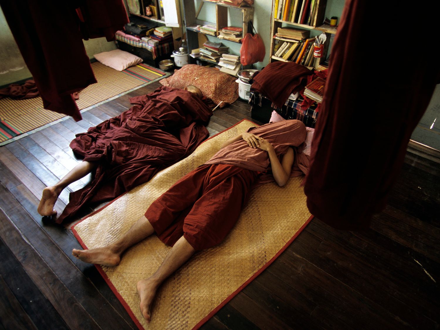 Buddhist monks in red robes lying prostrate on wooden floor during prayer meditation practice.
