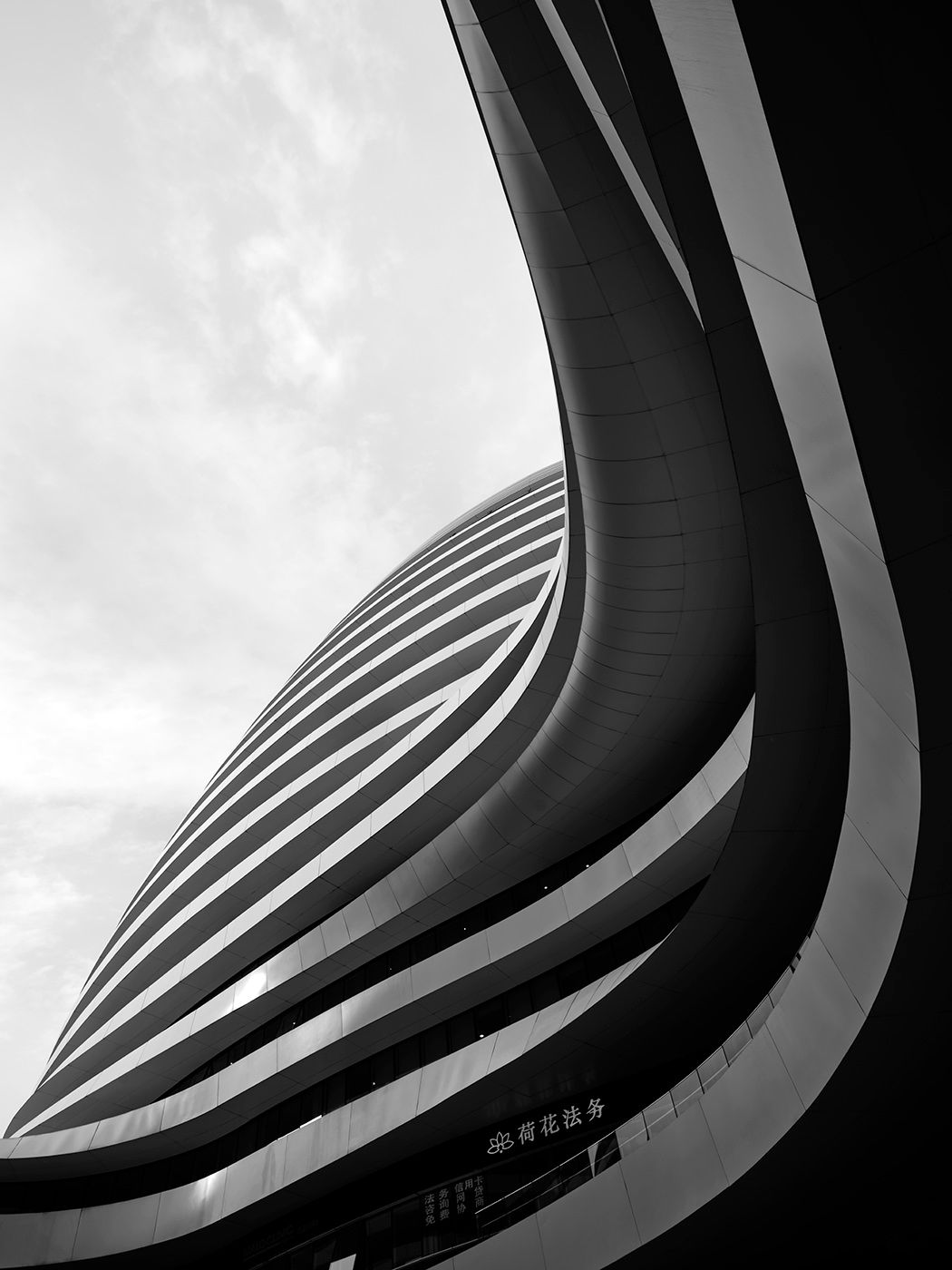 Black and white low-angle shot of a modern curved skyscraper with striped facade against cloudy sky.