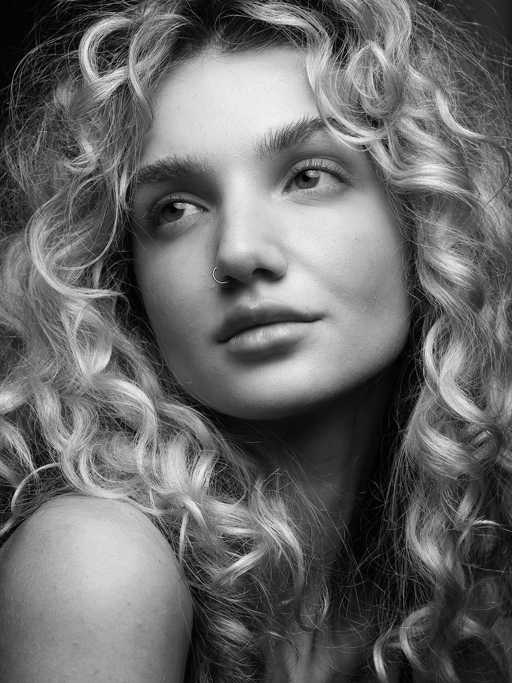 Black and white portrait of a young woman with voluminous curly blonde hair, gazing softly at the camera.