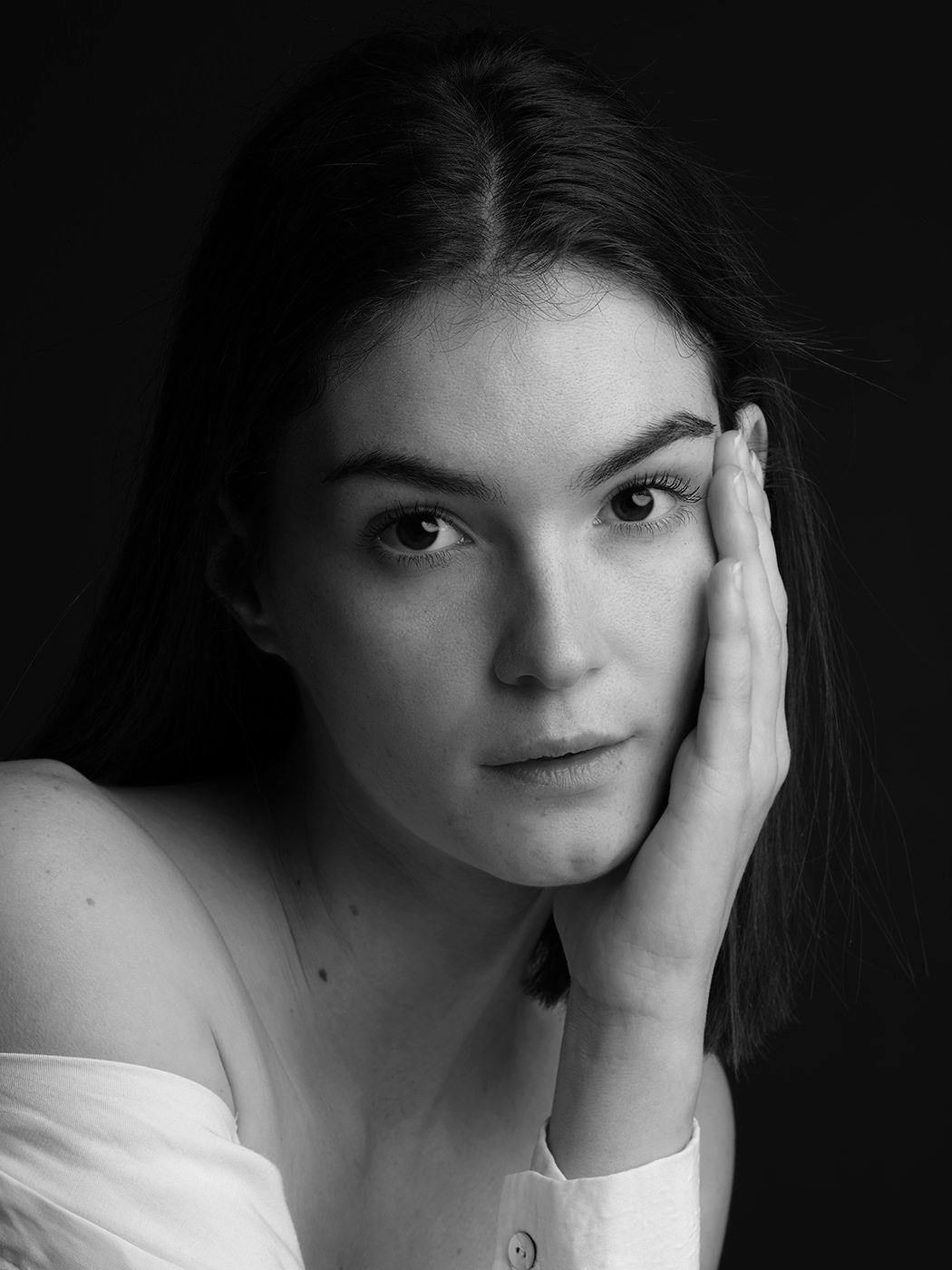 Black and white portrait of a young woman resting her hand on her cheek, gazing softly at the camera.