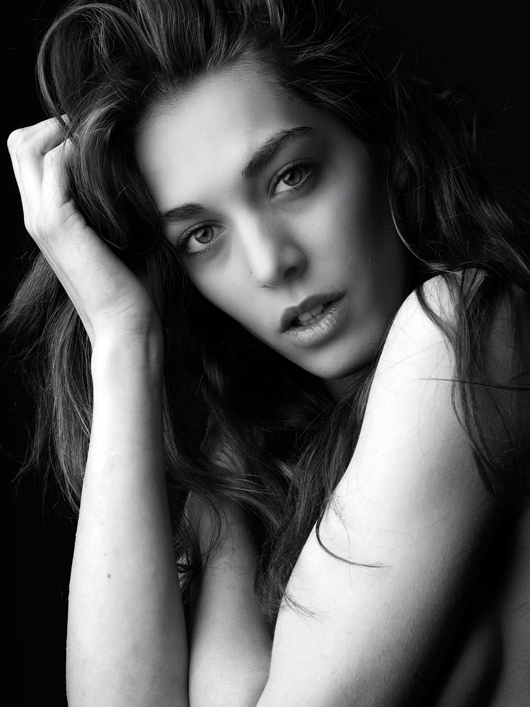 Black and white portrait of a young woman with long hair posing gracefully against a dark background.