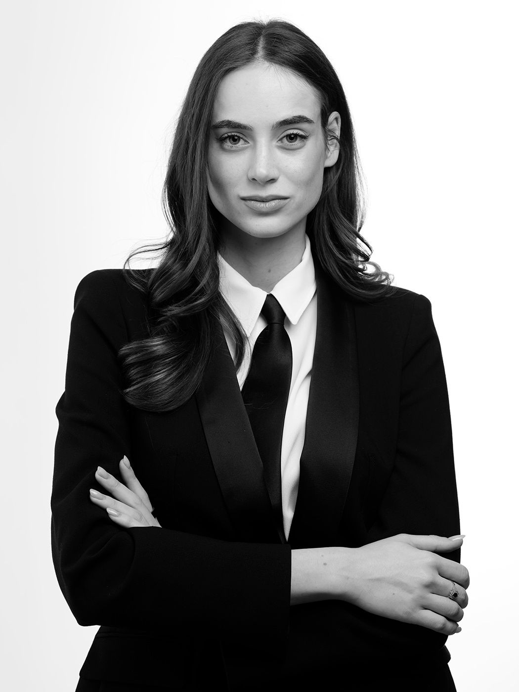 Black and white portrait of a woman in a black blazer and tie with arms crossed.