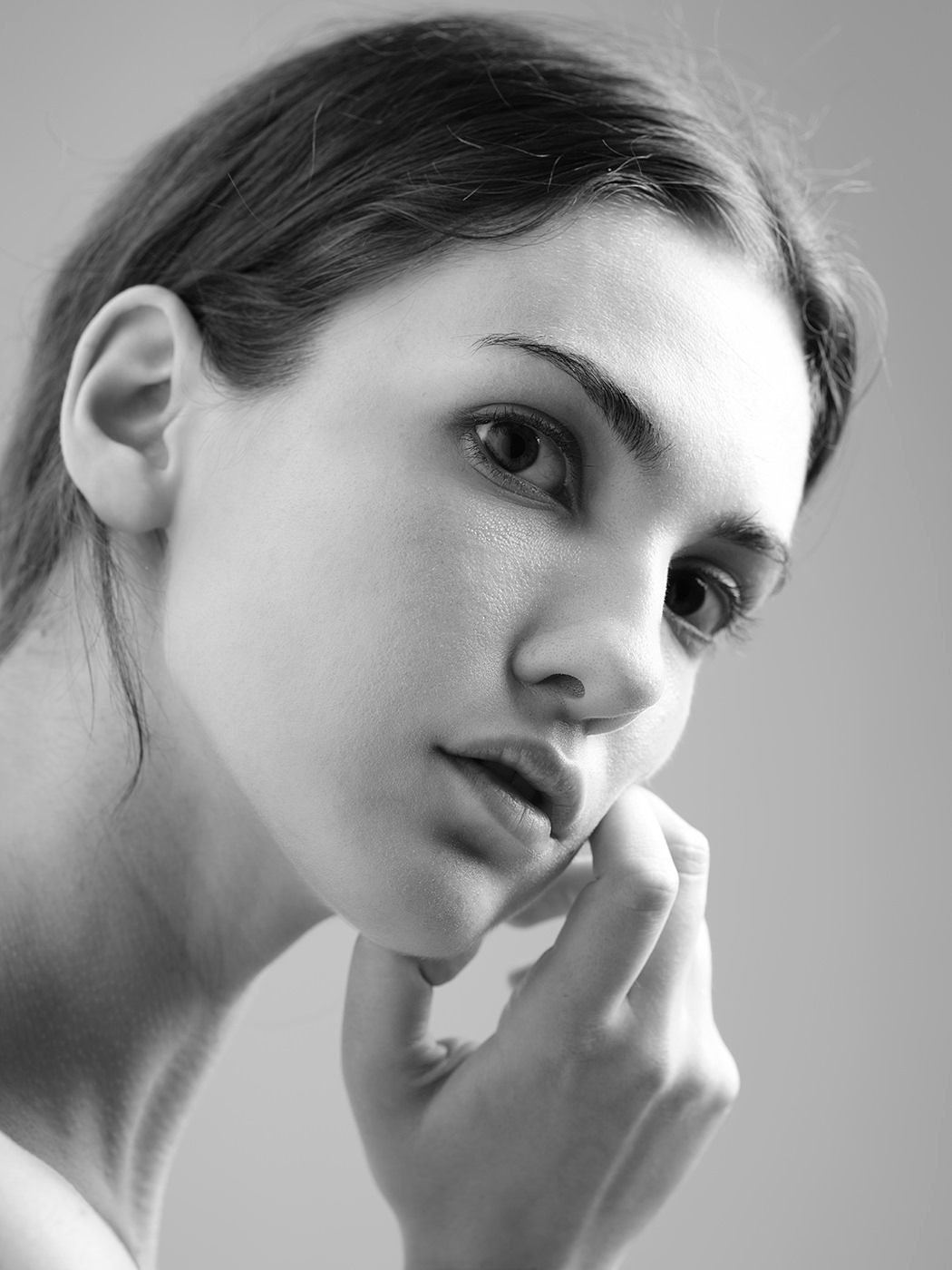 Black and white portrait of a young woman resting her chin on her hand, gazing thoughtfully to the side.
