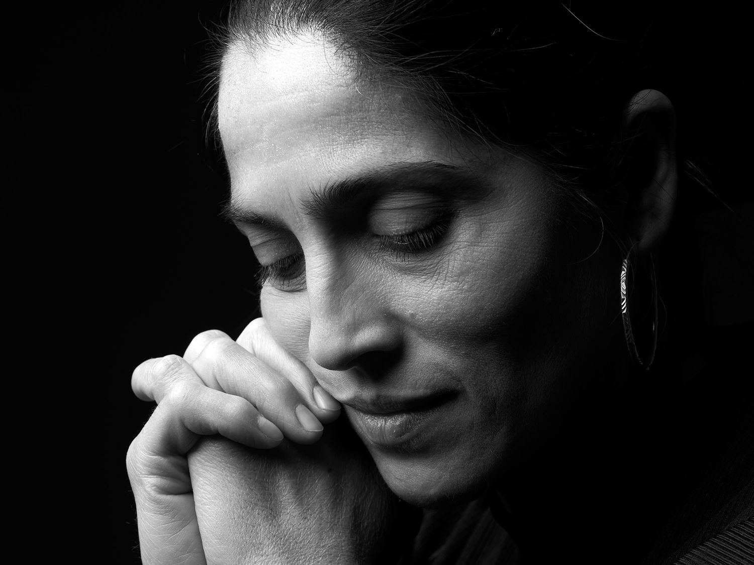 Black and white portrait of a woman with closed eyes and hands clasped in prayer, conveying peace and reflection. Lakatos Mónika