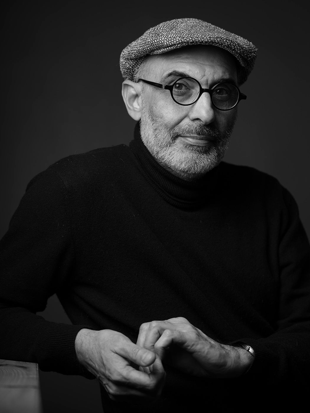 Black and white portrait of an older man wearing a flat cap, glasses, and turtleneck sweater.