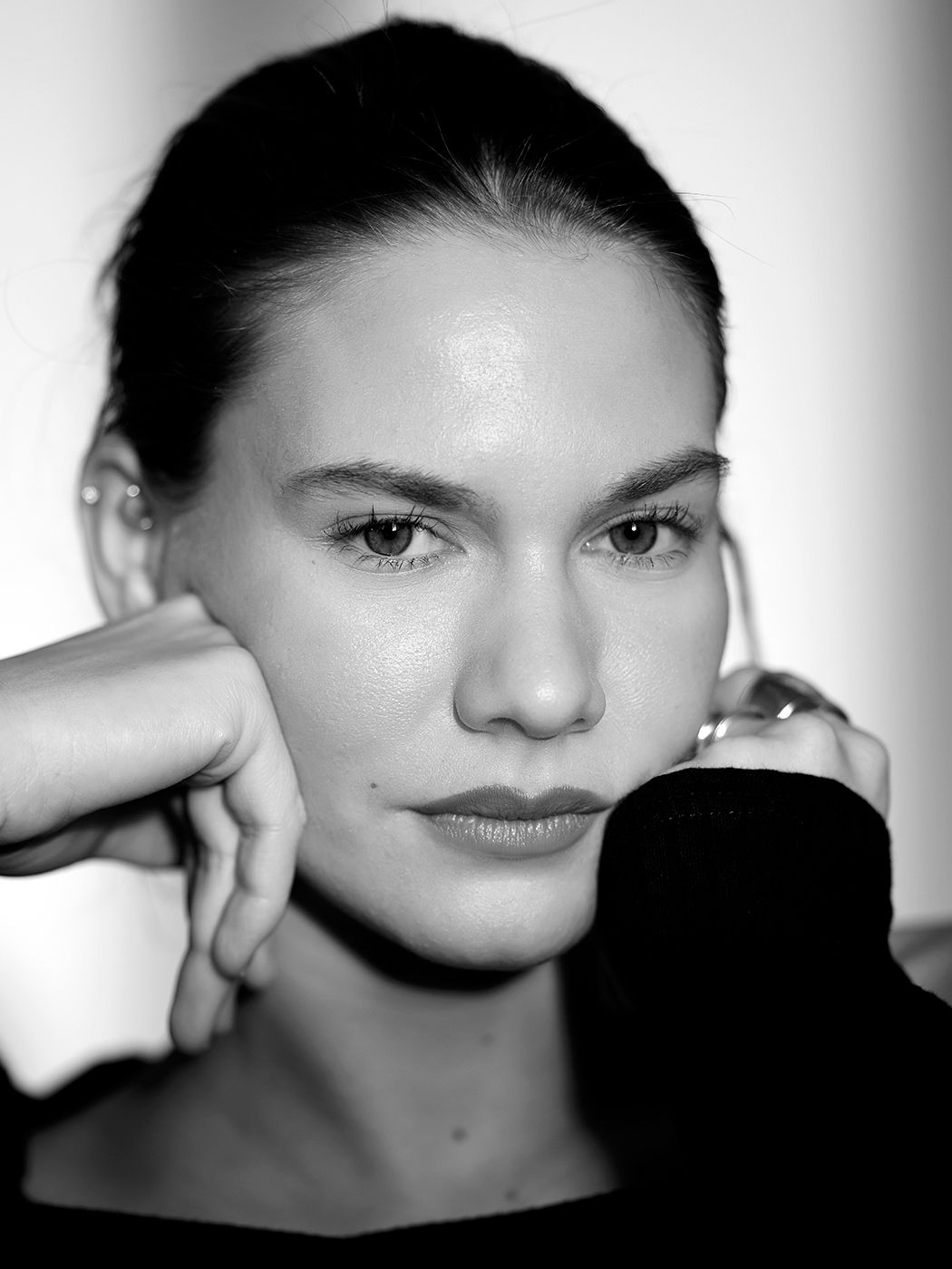 Black and white close-up portrait of a young woman with dark hair pulled back, resting her hand near her face.