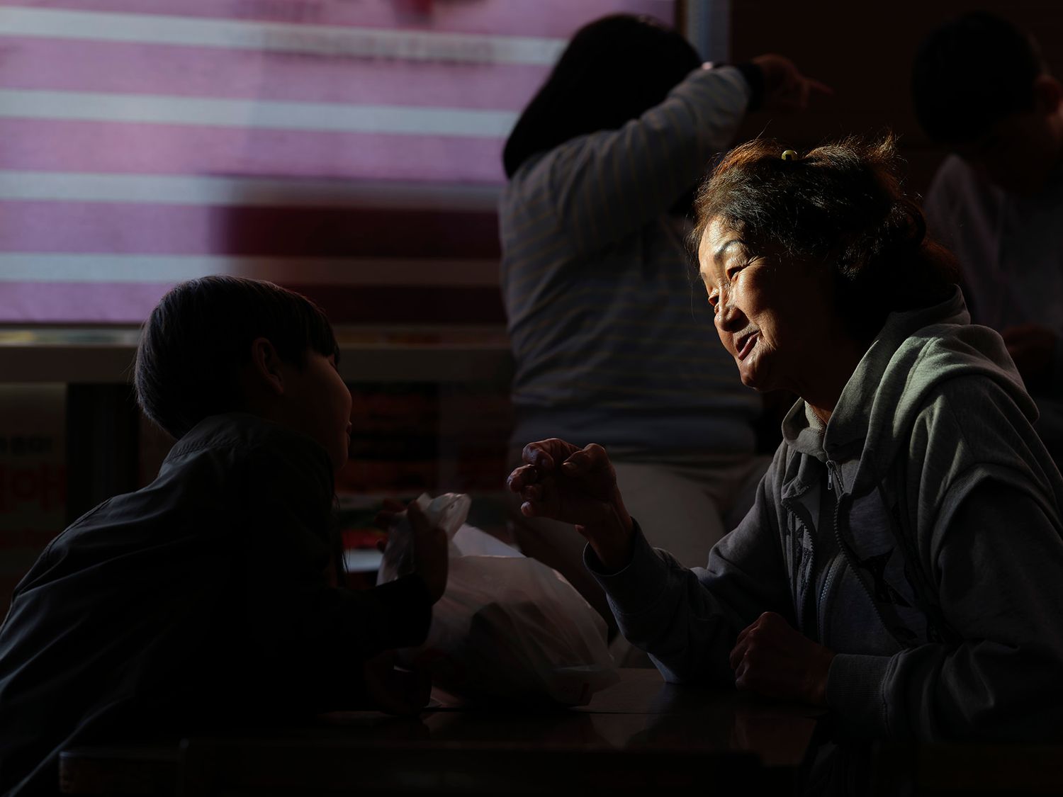 Two people share an intimate conversation at a dimly lit table, with soft pink striped light in the background.