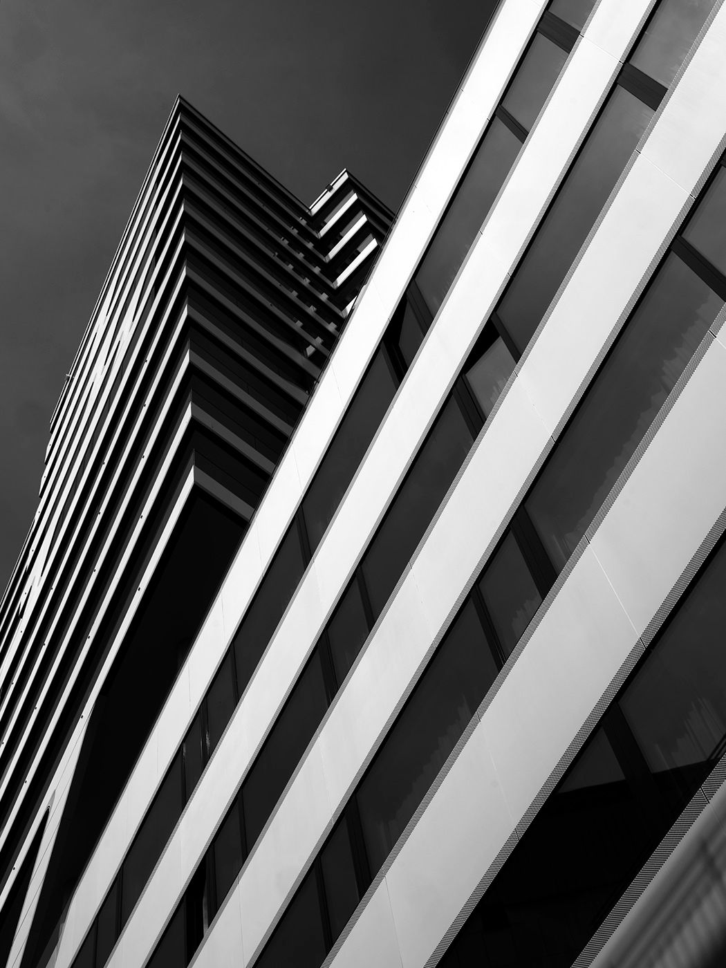 Black and white low-angle shot of modern skyscrapers with bold geometric lines and glass facades against a dramatic sky.