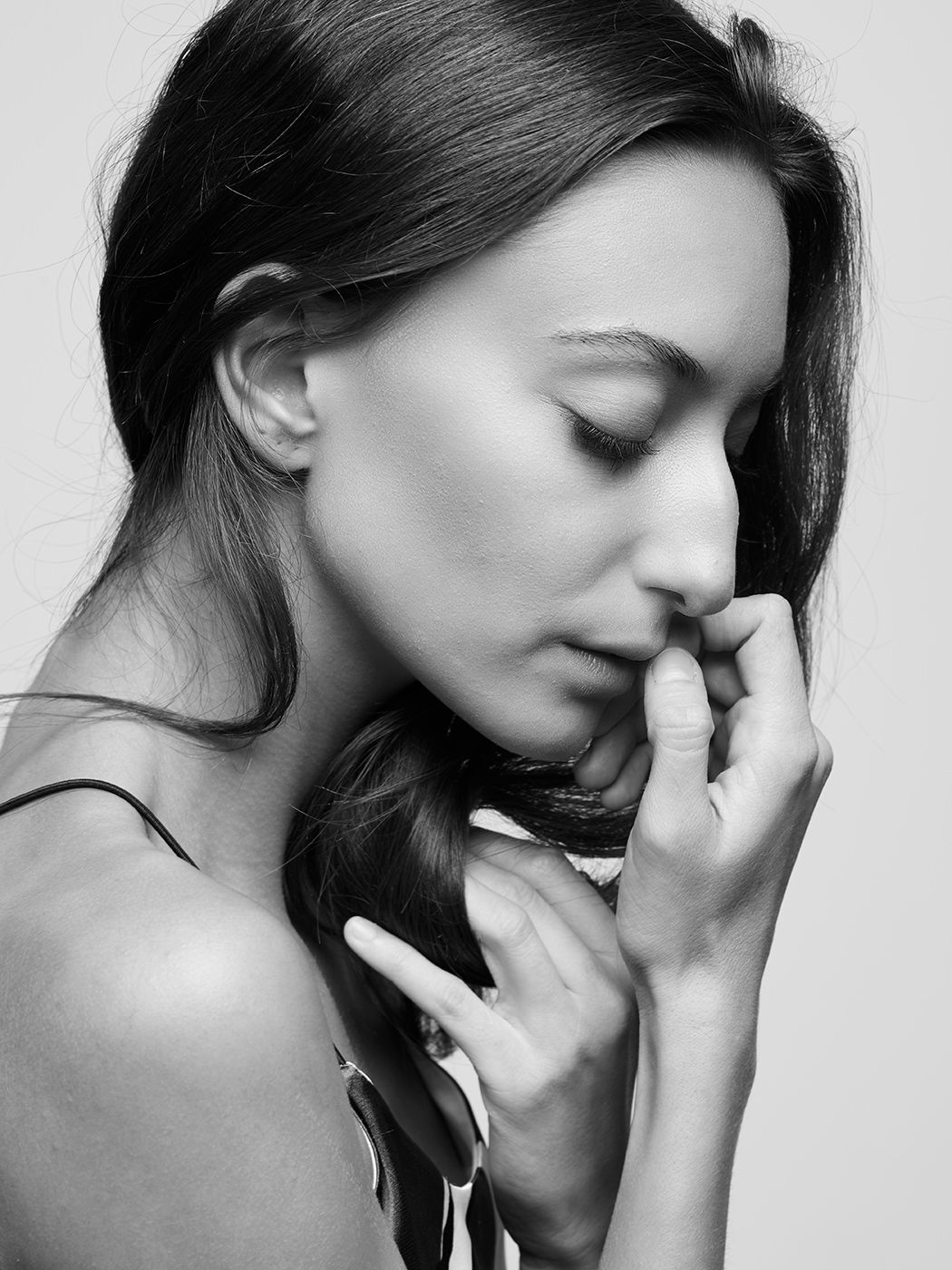 Black and white portrait of a young woman with closed eyes, hand near face, wearing a ring and floral top.