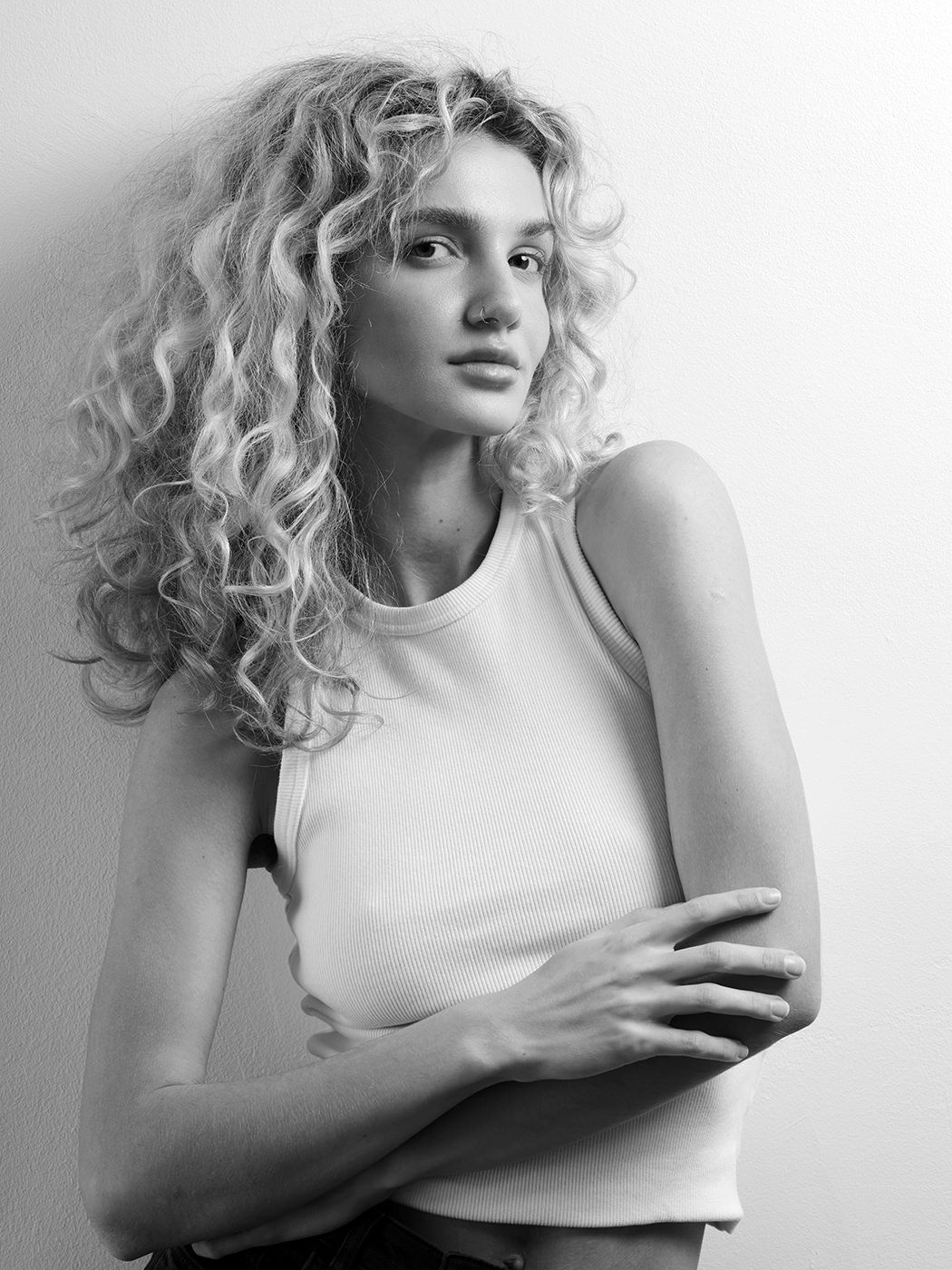 Black and white portrait of a young woman with curly blonde hair wearing a white crop top, arms crossed.