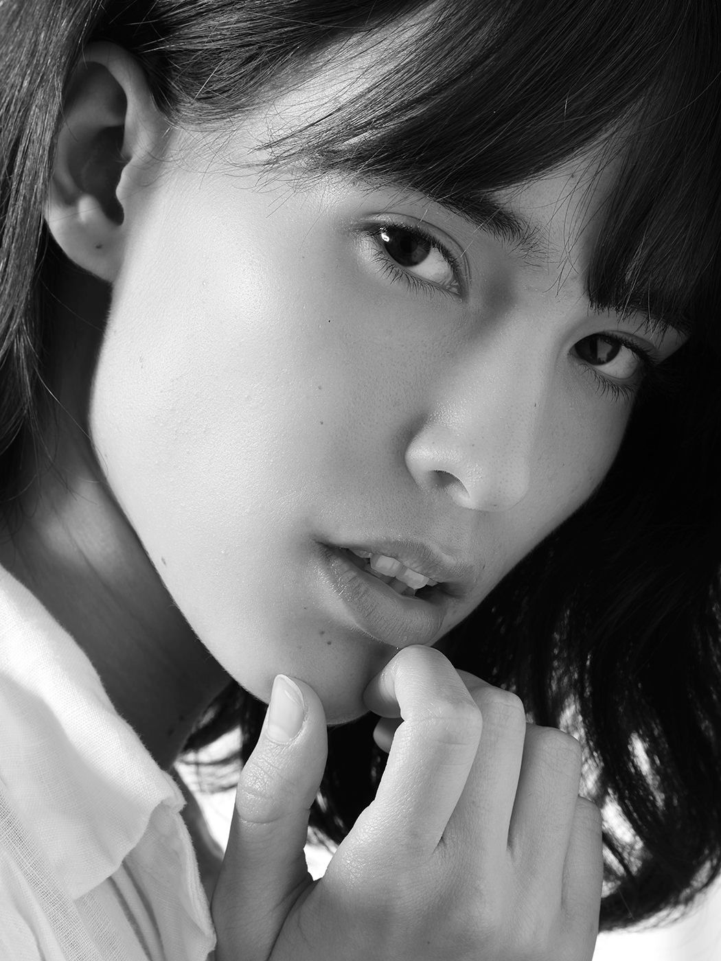Black and white portrait of a young woman with dark hair, hands clasped near chin, gazing at camera.