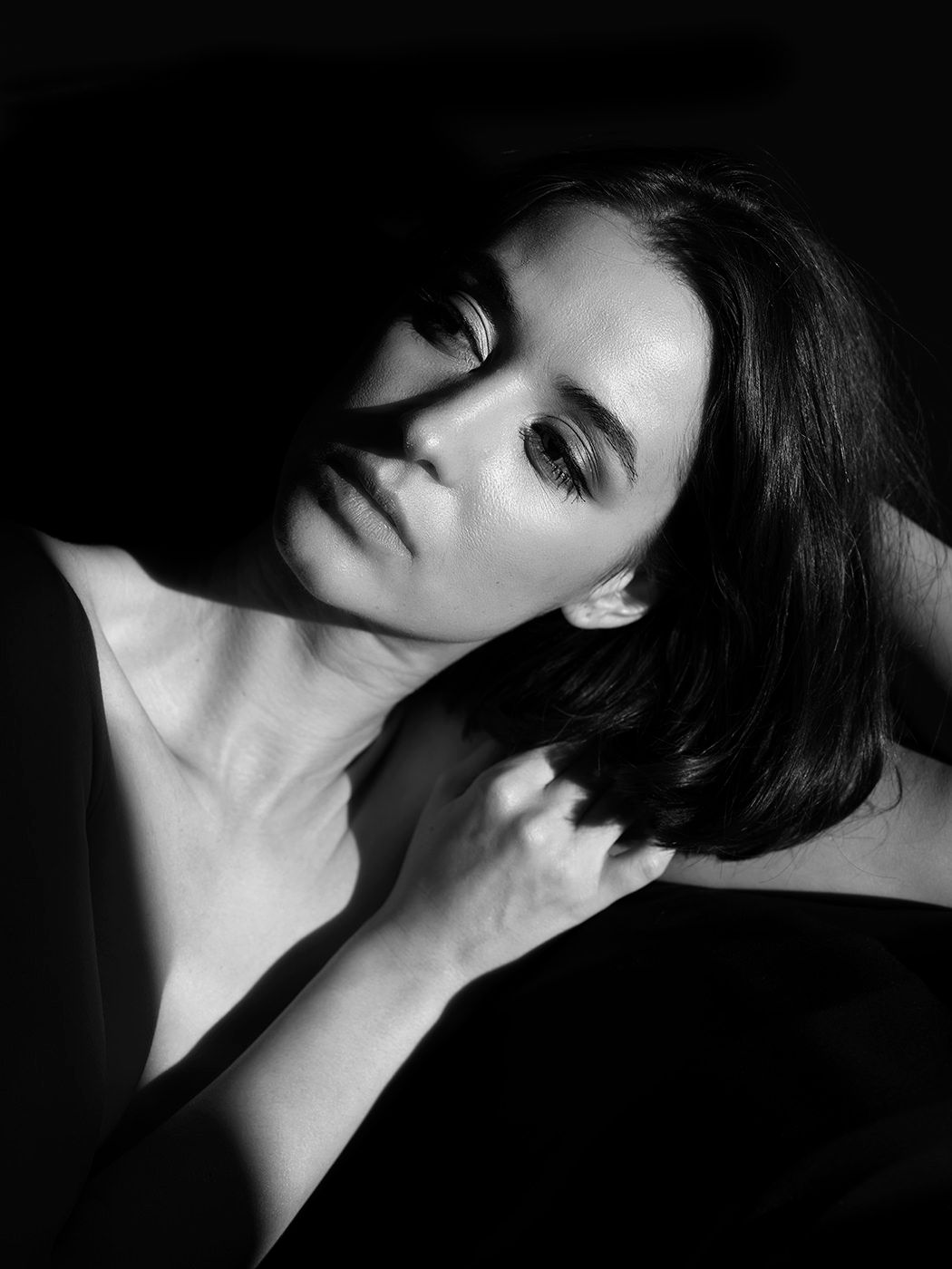 Black and white dramatic portrait of a dark-haired woman with moody lighting and hand on chest.
