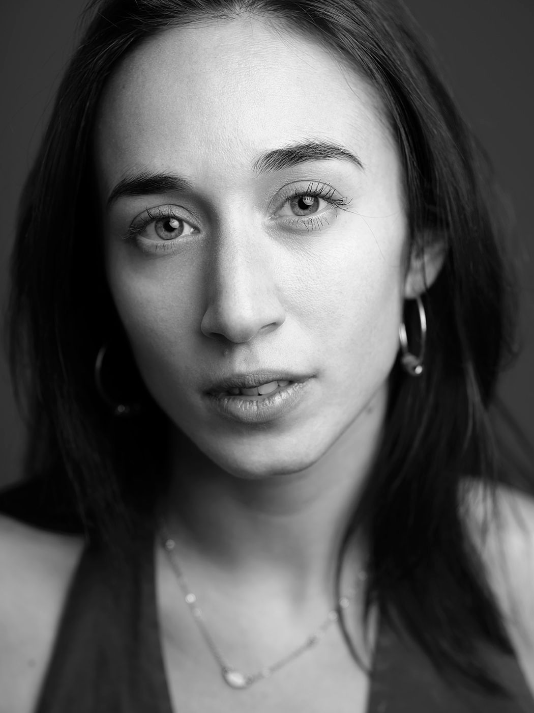 Black and white close-up portrait of a young woman with dark hair wearing hoop earrings and a necklace.