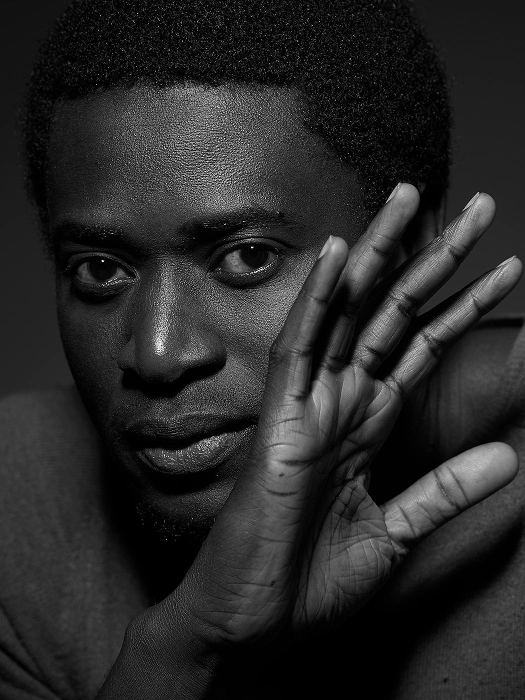 Black and white portrait of a young man resting his face against his raised hand, looking directly at camera. Alune Wade