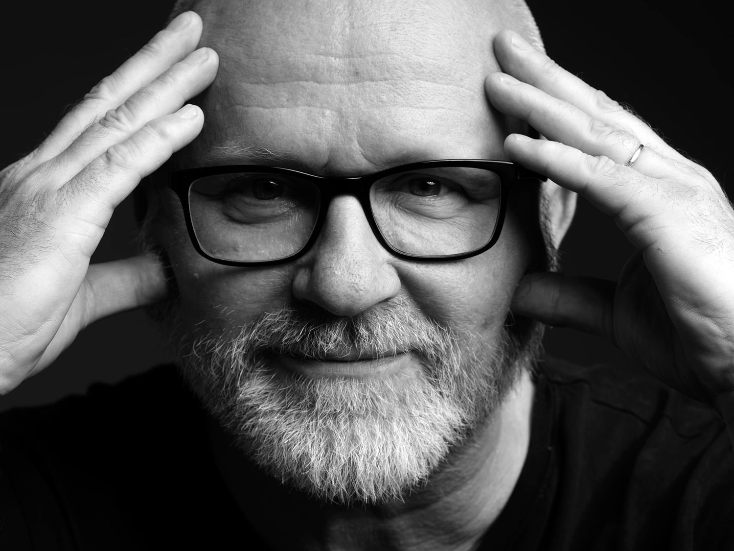 Black and white portrait of a bald man with glasses and beard, hands on temples, thoughtful expression. Prieger Zsolt, musician.