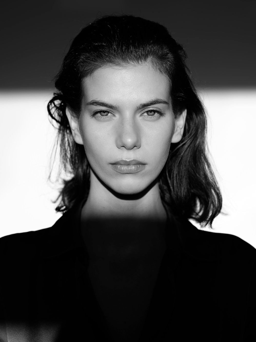 Black and white close-up portrait of a young woman with shoulder-length dark hair and striking features.