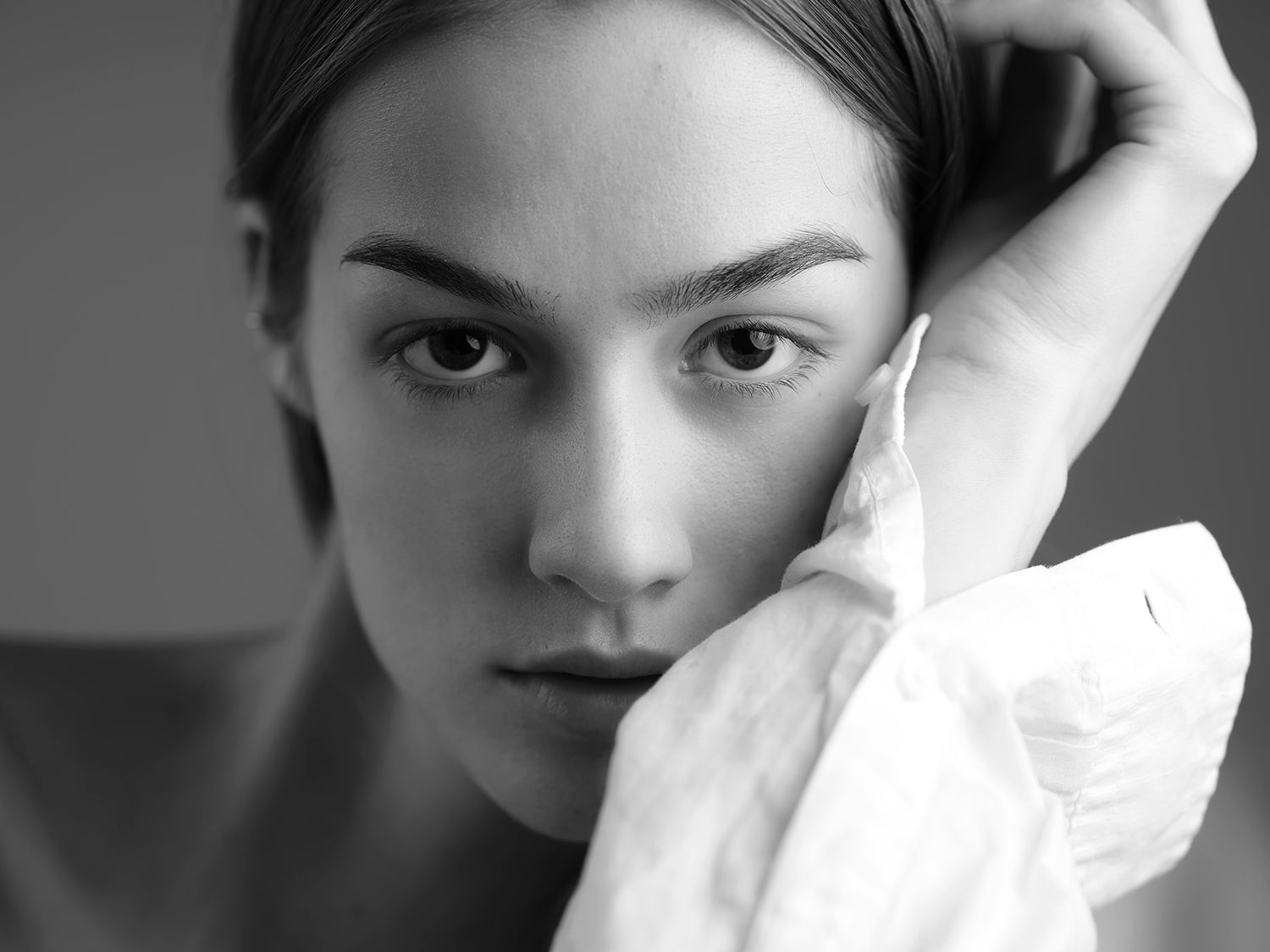 Black and white portrait of a young woman holding a white fabric, gazing intensely at the camera.