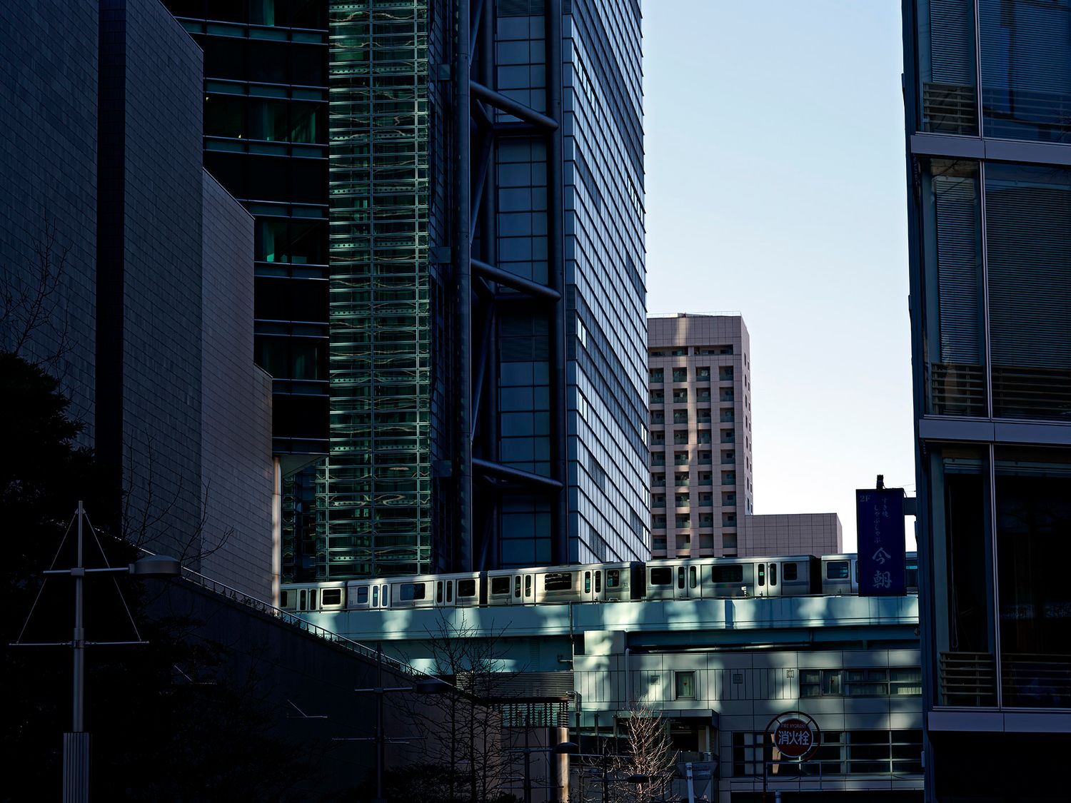 An elevated train passes between modern glass skyscrapers in an urban city downtown district at dusk.