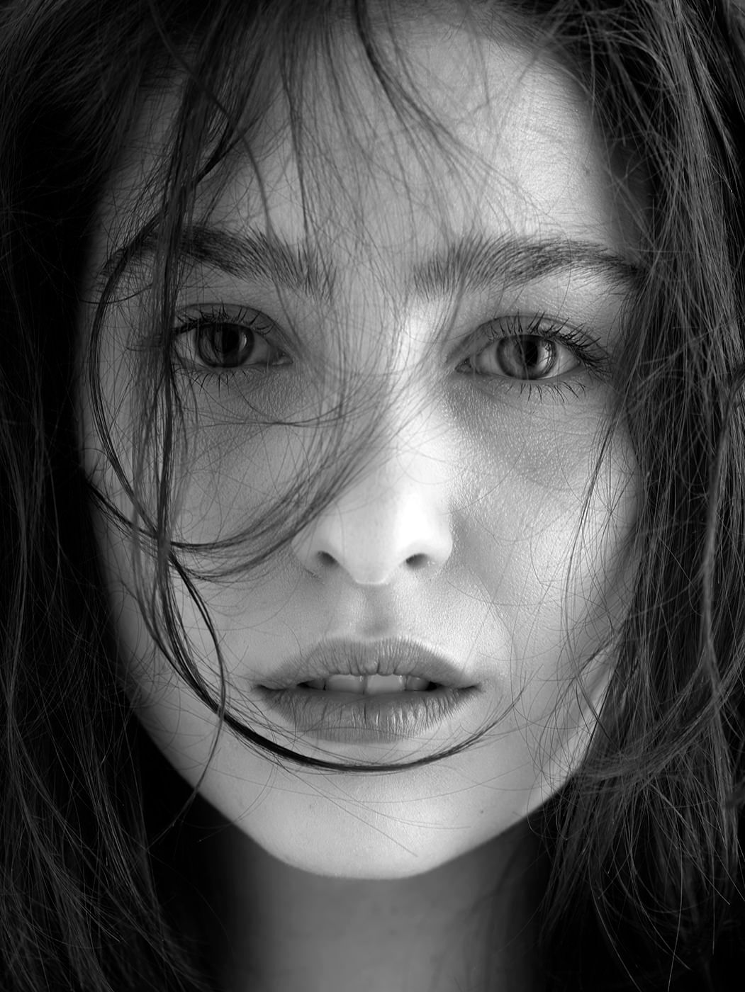 Close-up black and white portrait of a young woman with windswept dark hair partially covering her face.