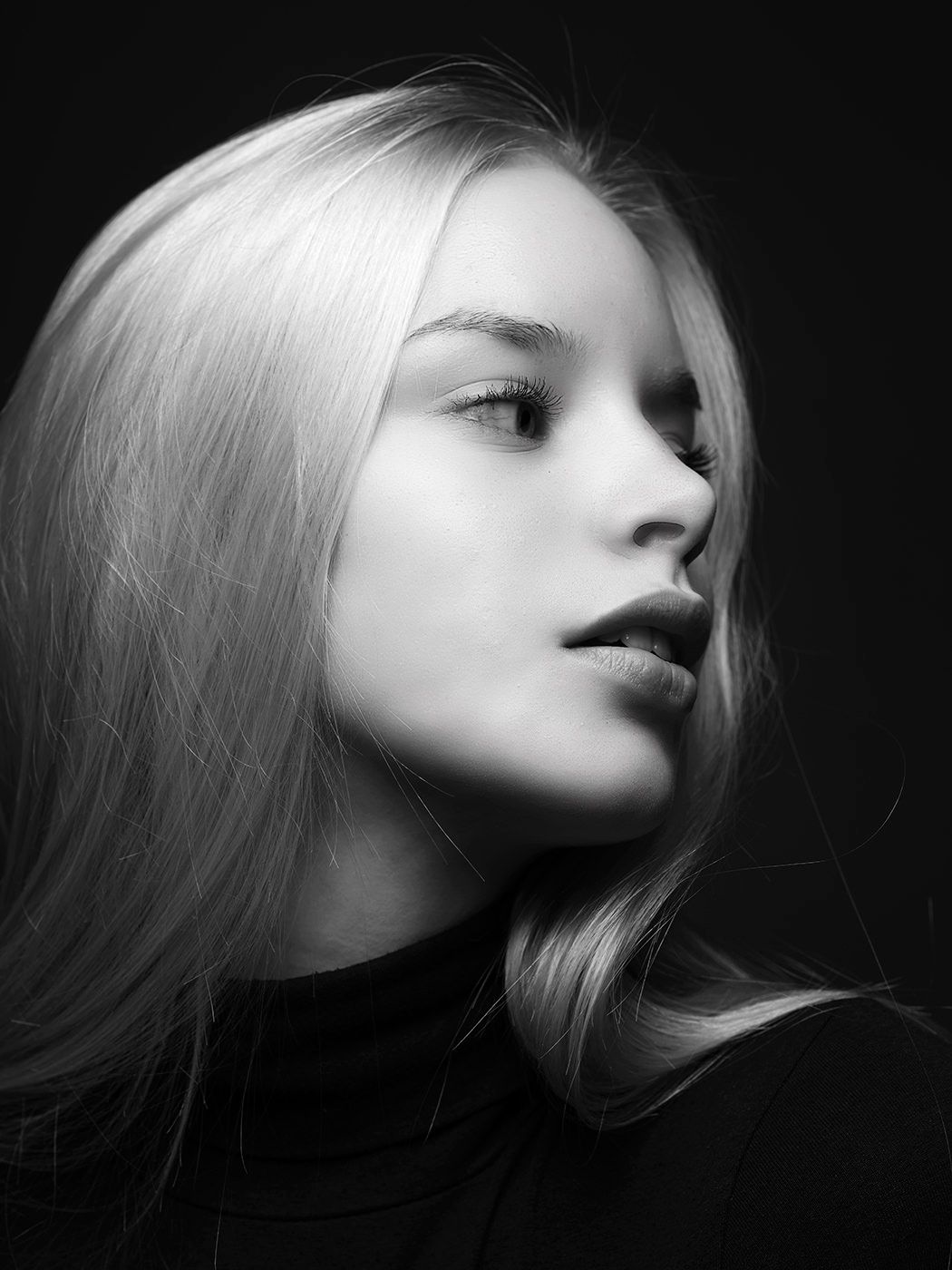 Black and white portrait of a young blonde woman in a turtleneck, dramatic studio lighting.