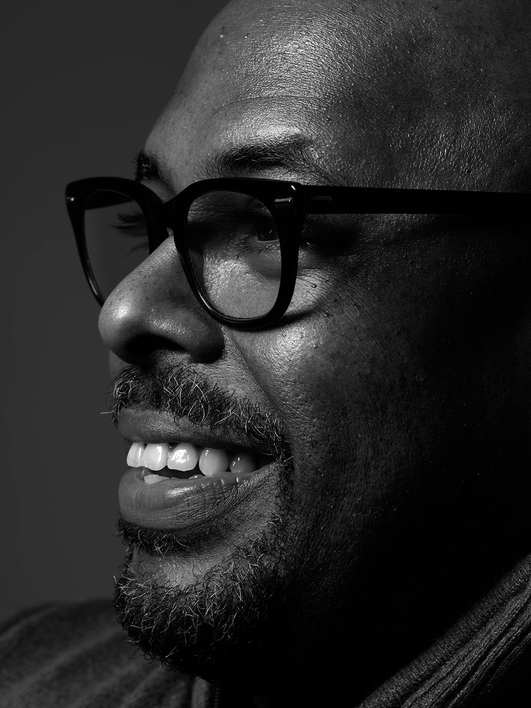 Black and white close-up portrait of a smiling bald man wearing bold black-framed glasses. Christian McBride