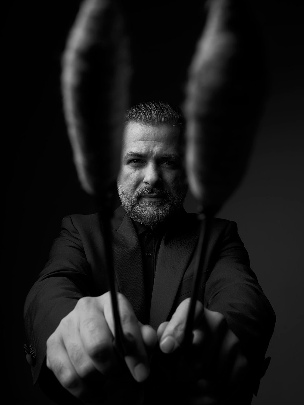 Black and white portrait of a bearded man in a suit holding drumsticks toward the camera with dramatic lighting. Lukács Miklós, cimbalom