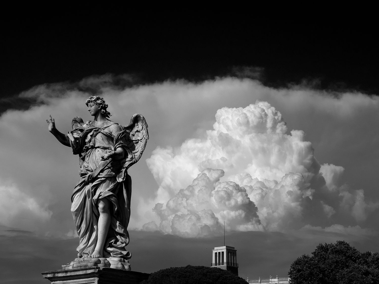 Black and white photo of an angel statue against dramatic storm clouds in Rome.